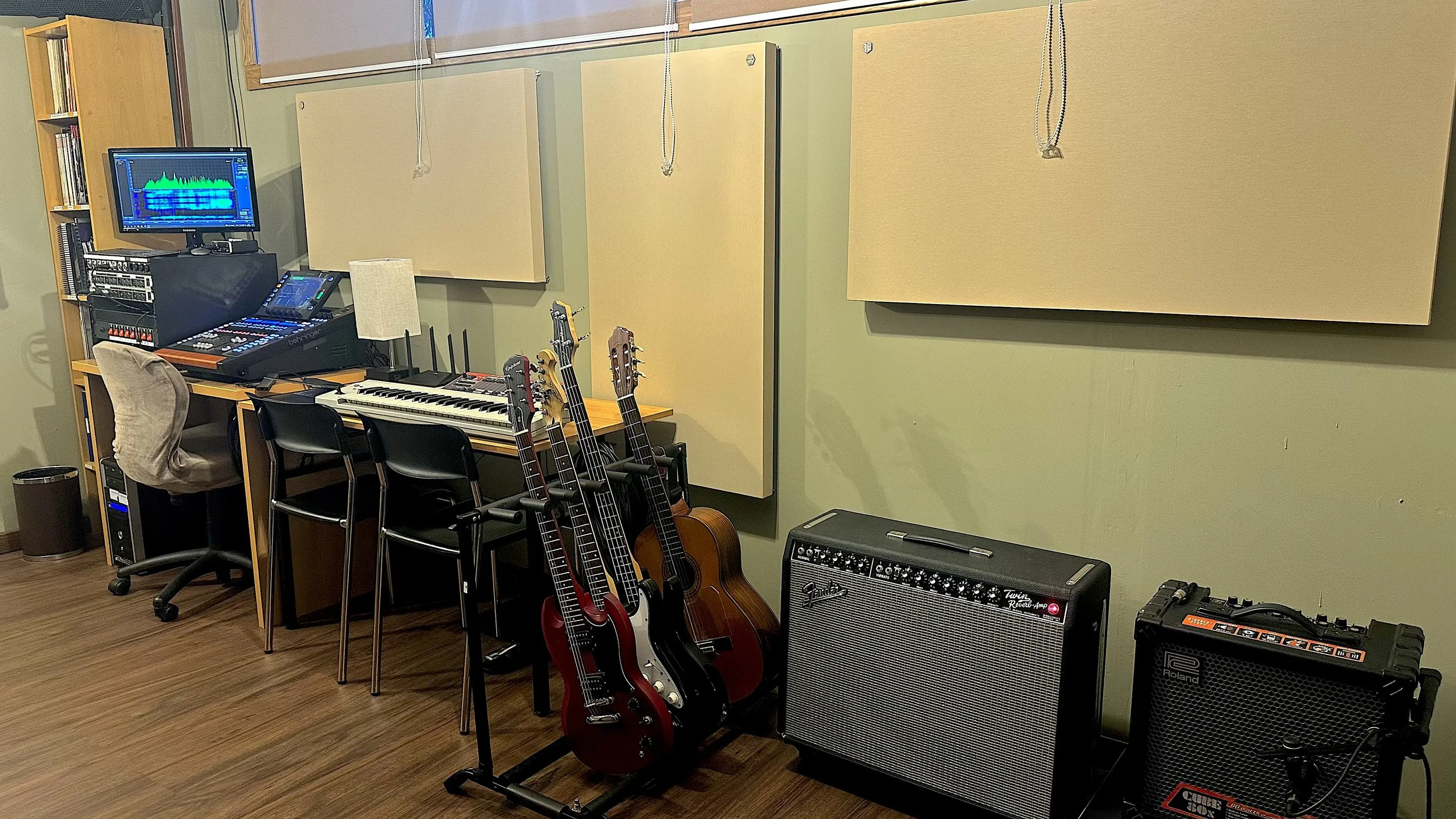 Estudio de música con guitarras eléctricas y acústicas, amplificadores, teclado, computadora con software de audio, y paneles acústicos en la pared.