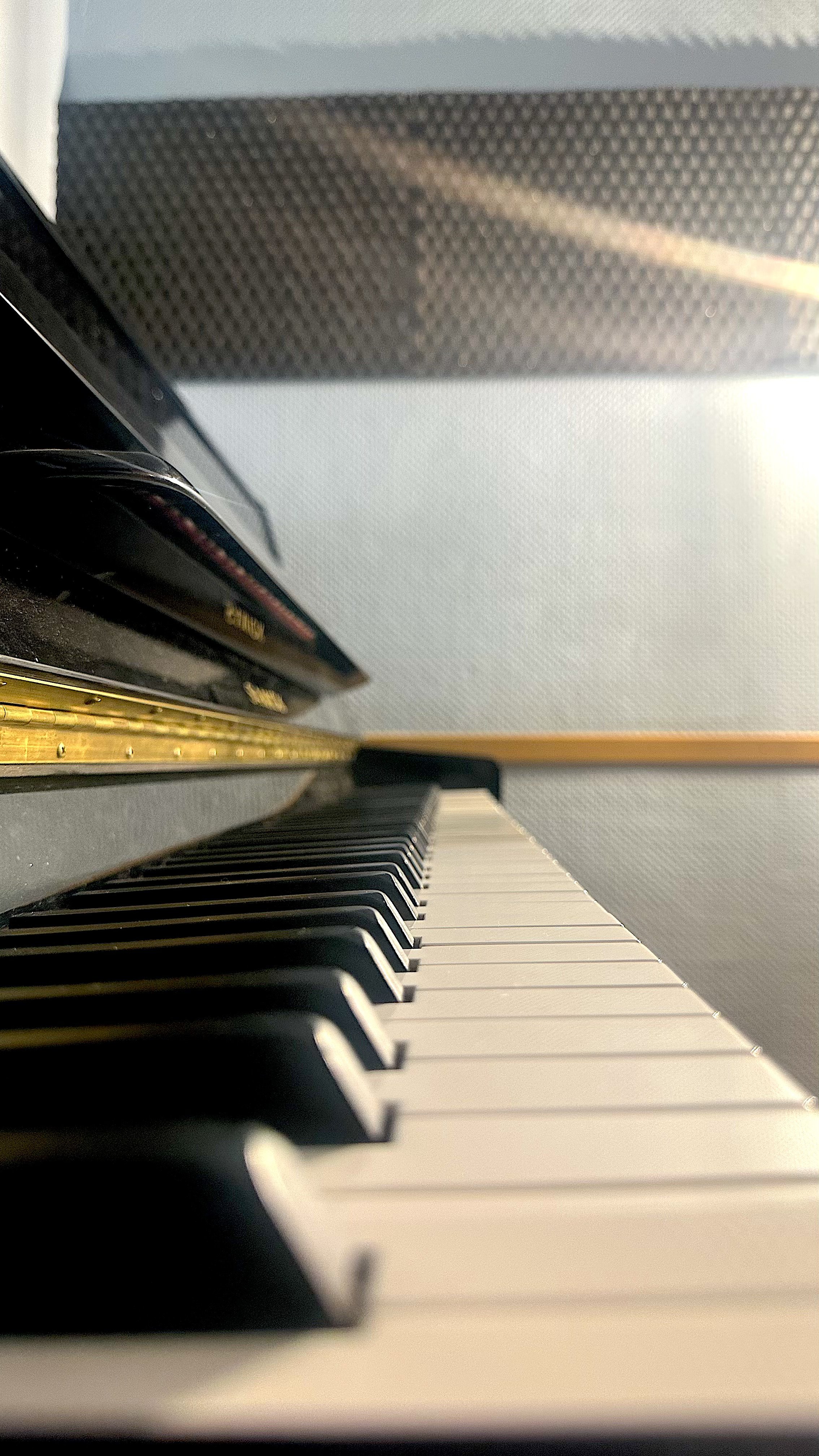 Vista del teclado de un piano desde abajo, con un fondo difuso y la pared de la habitación.