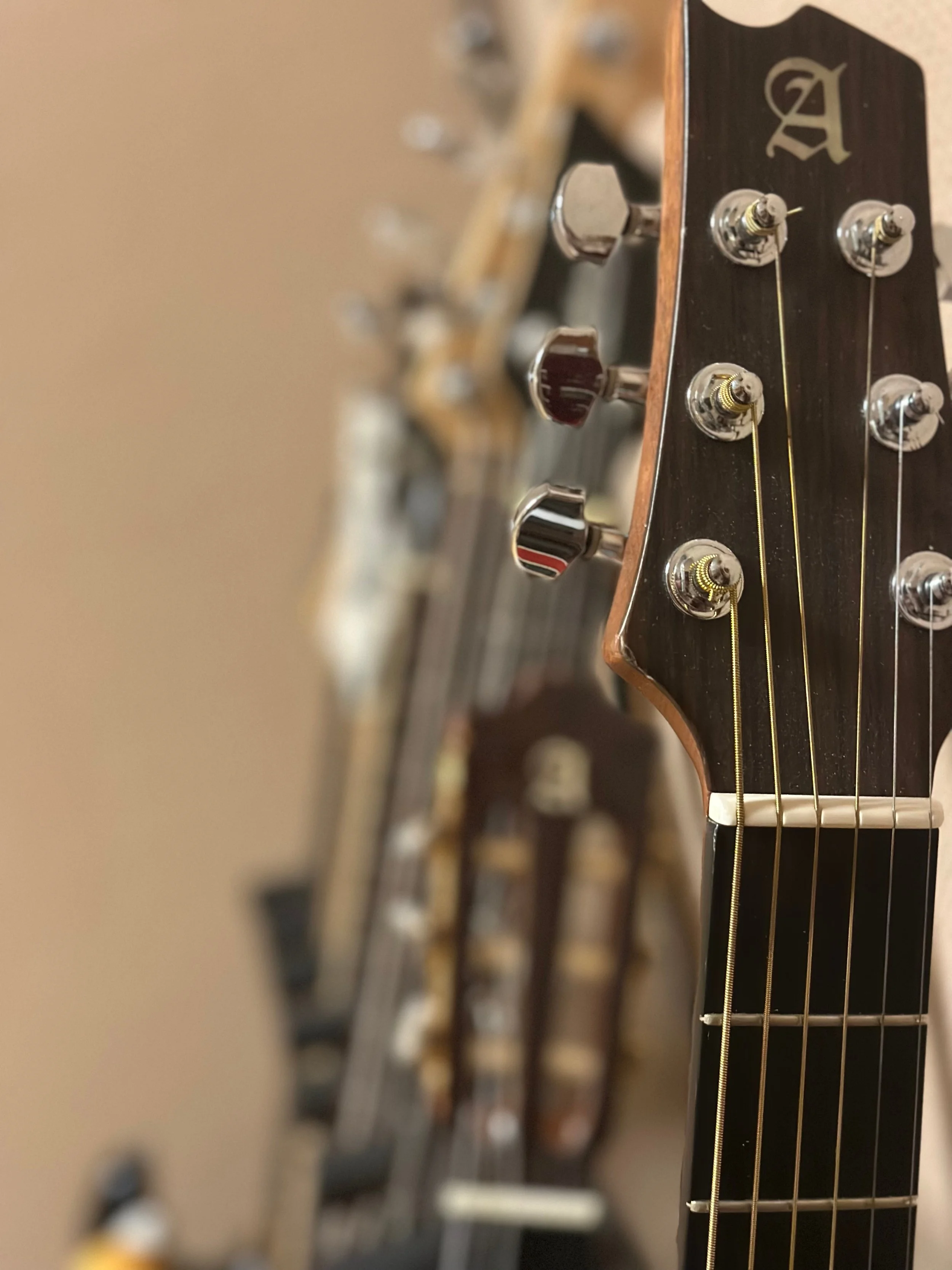 cabecera y clavijero de una guitarra acústica, con varias guitarras en el fondo.