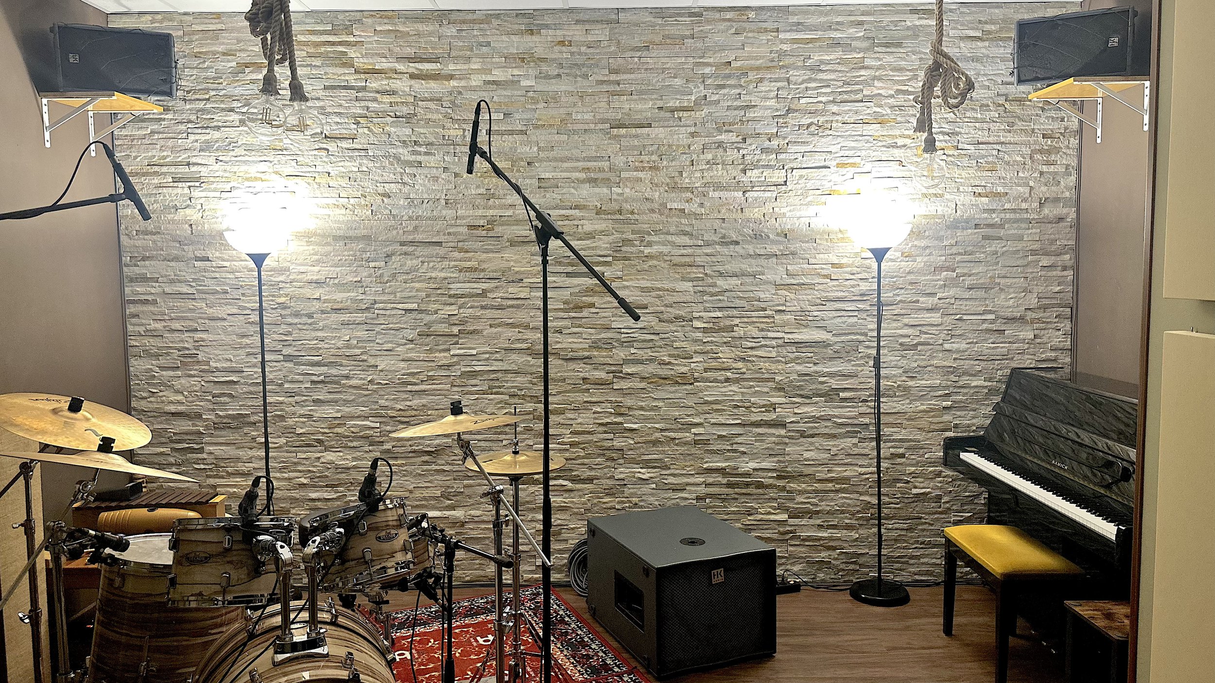 Estudio de música con batería, piano, micrófono, luces y altavoces.