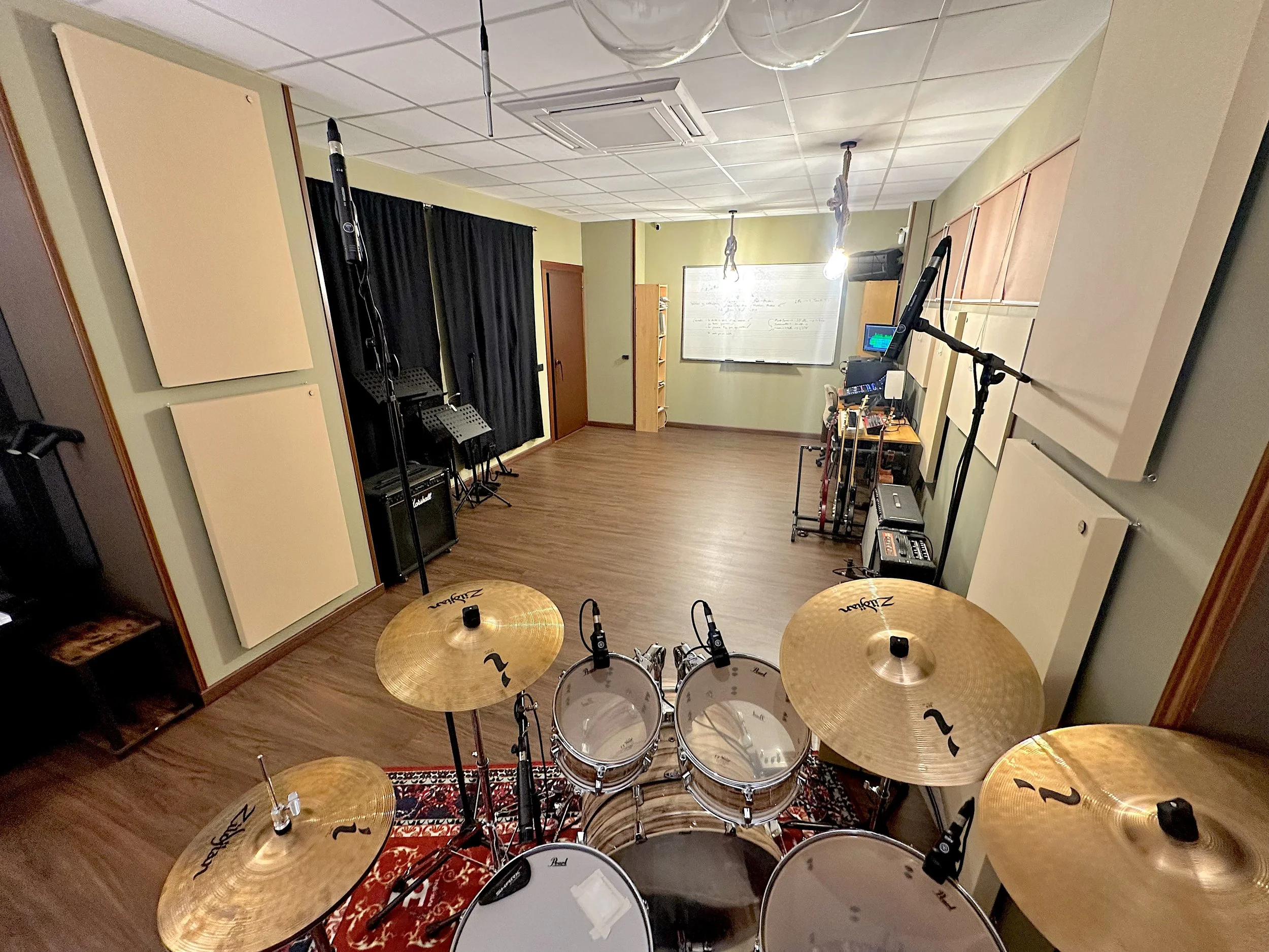 Sala de grabación o ensayo con batería, micrófonos, amplificadores y equipo musical, vista desde el escenario hacia la sala.