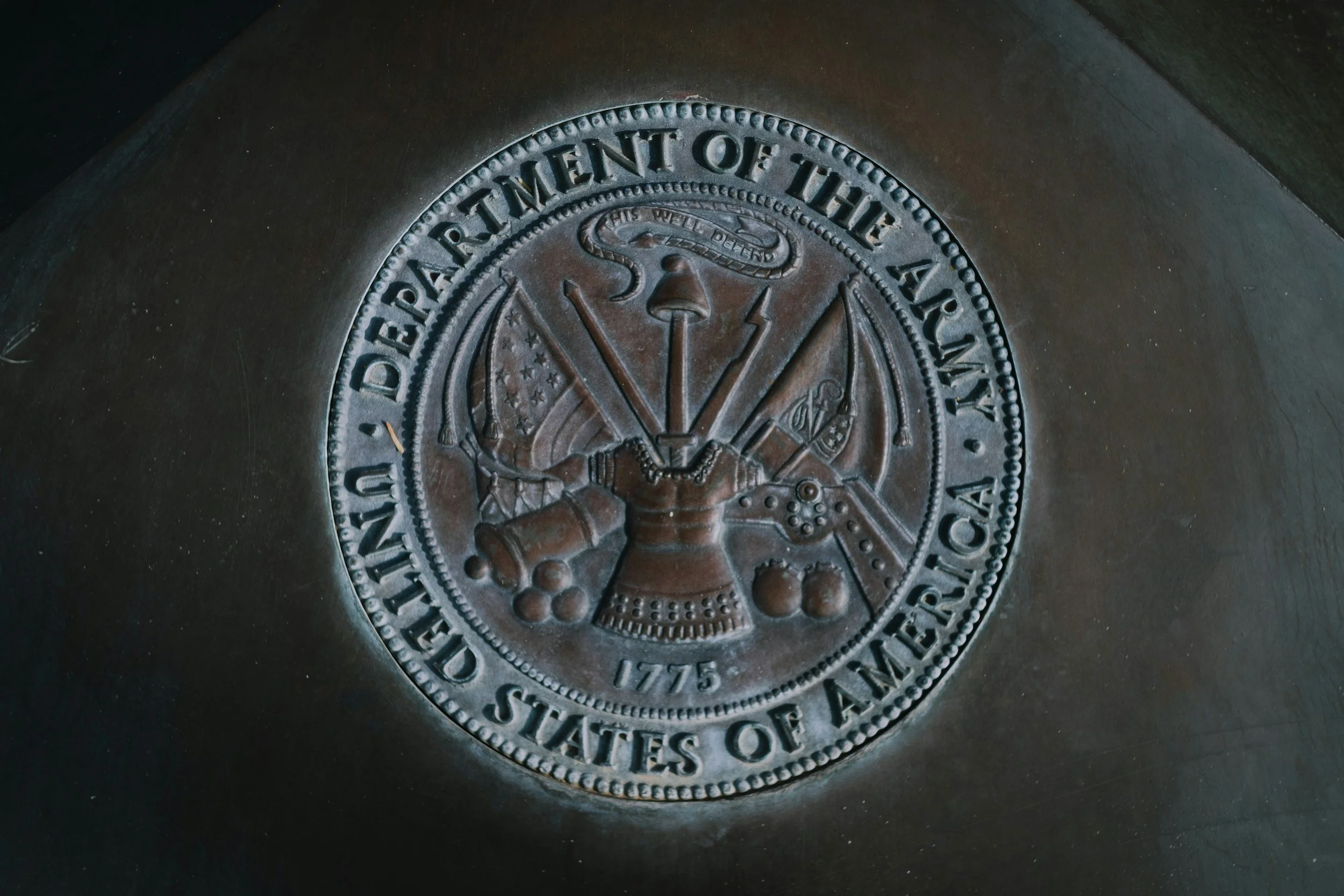 Sealed emblem of the United States Department of the Army with the inscription, 'United States Department of the Army' and the year 1775, featuring symbols of military weapons and tools.