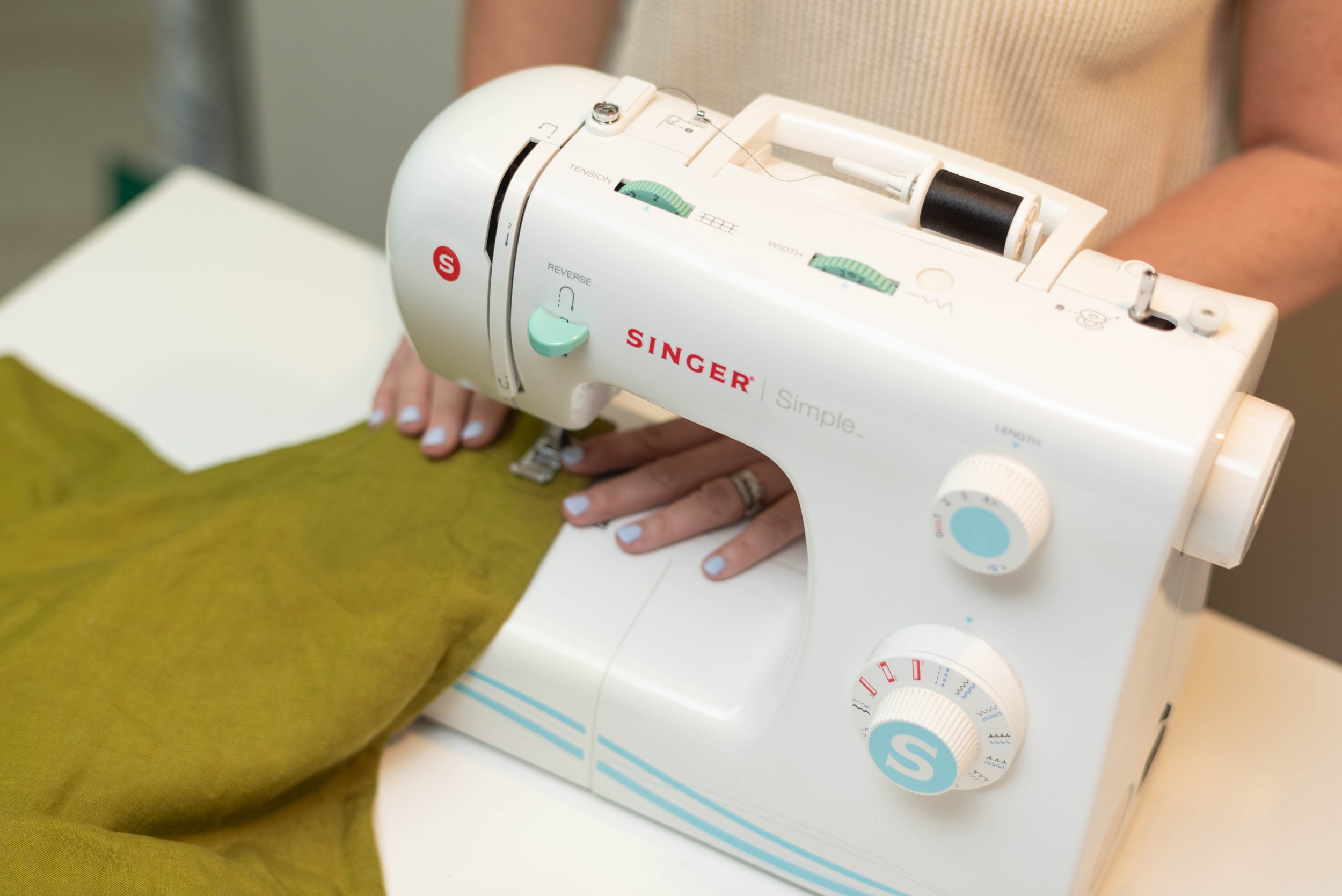 Person sewing green fabric with a Singer sewing machine.