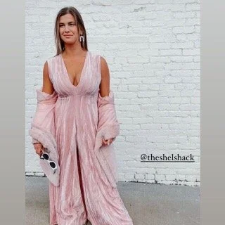 Woman in a pink and white dress holding sunglasses against a white brick wall