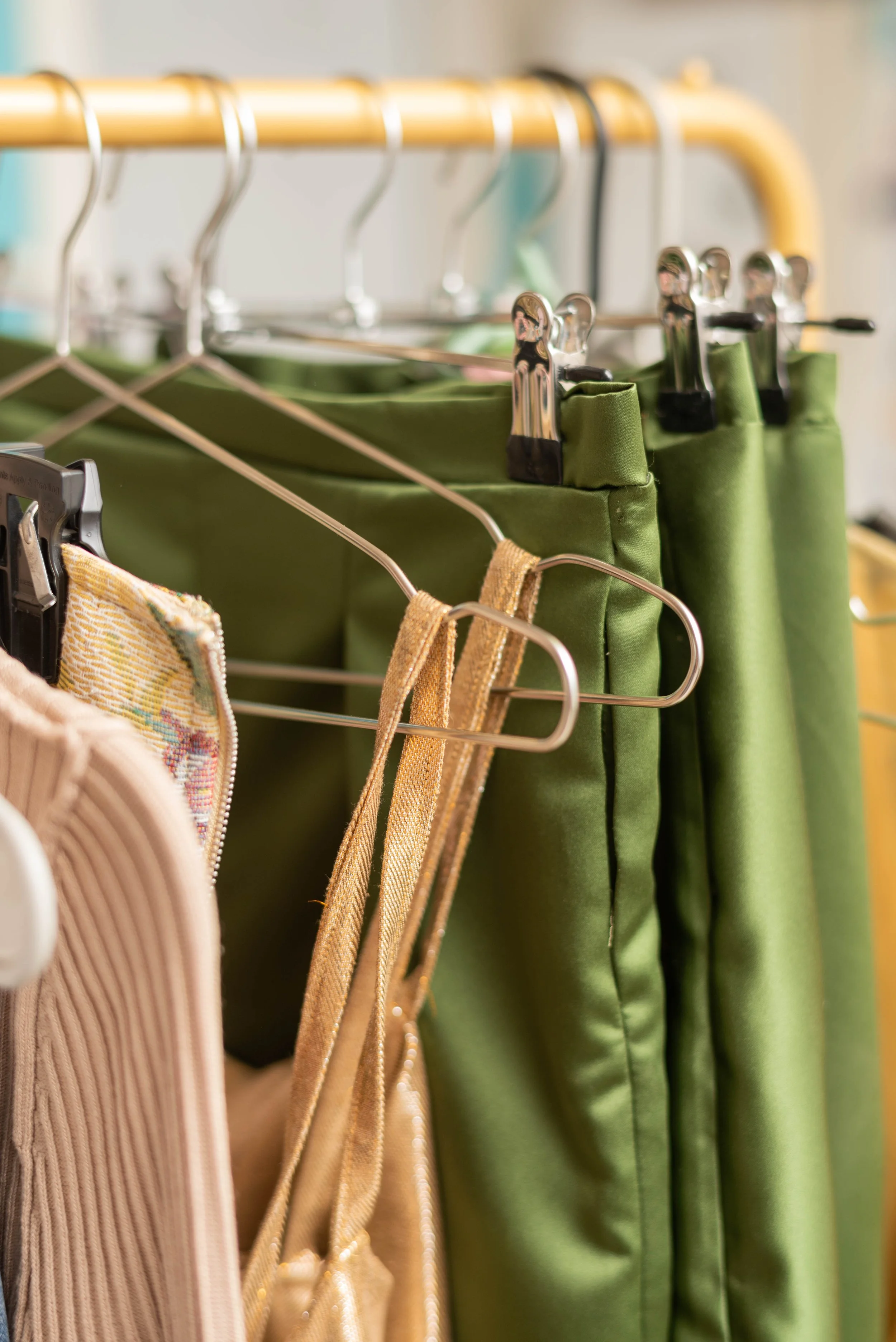 Close-up of a clothing rack with green pants and other garments hanging on metal and wooden hangers.