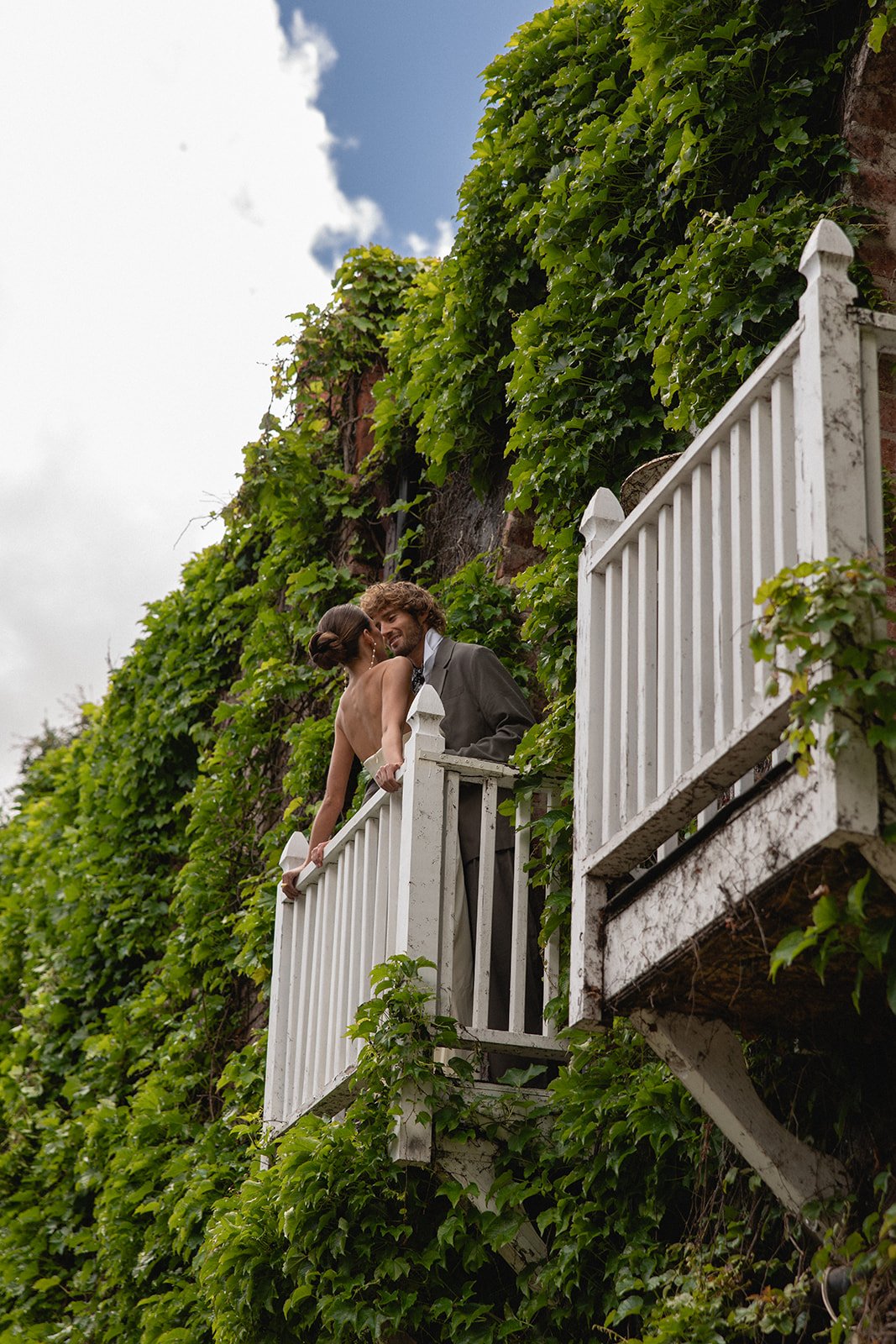 A bride and groom standing on Romeo and Juliet balcony surrounded by green ivy, sharing an intimate moment outdoors at 1880 Union Hotel Bridal dressing room in california.