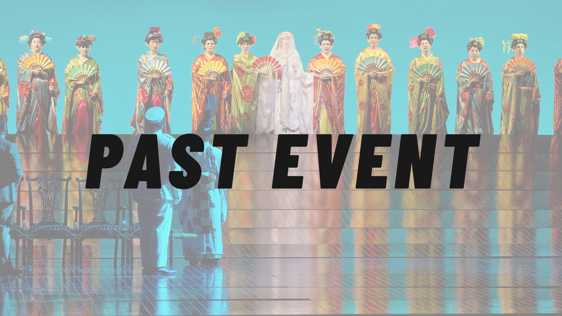 The image shows a stage with twelve women dressed in colorful traditional kimonos and umbrellas, standing in a line. In the foreground, three men in different costumes are observing the display.