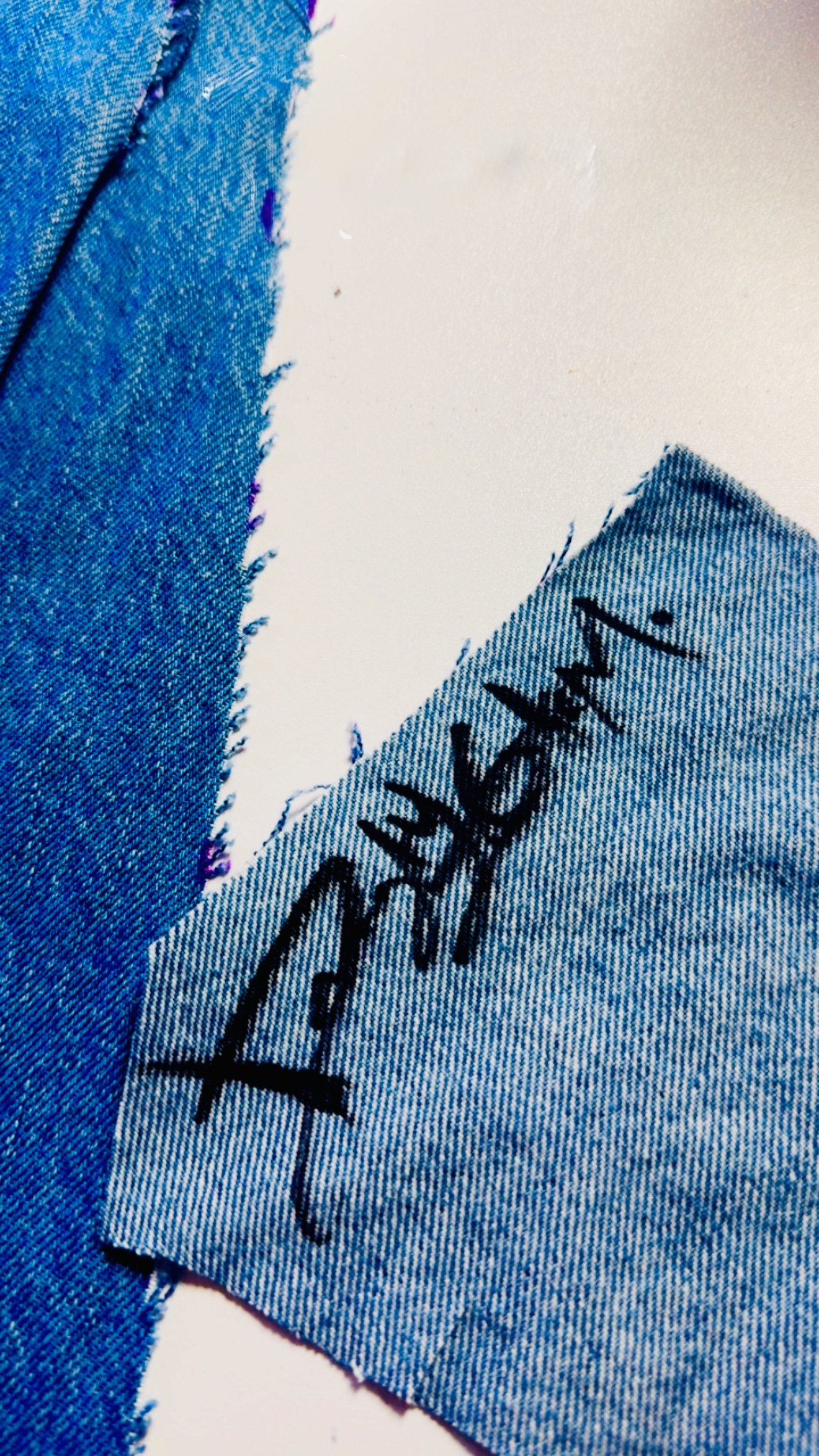 Close-up of a denim fabric patch with blue stitching and a black handwritten signature on it.