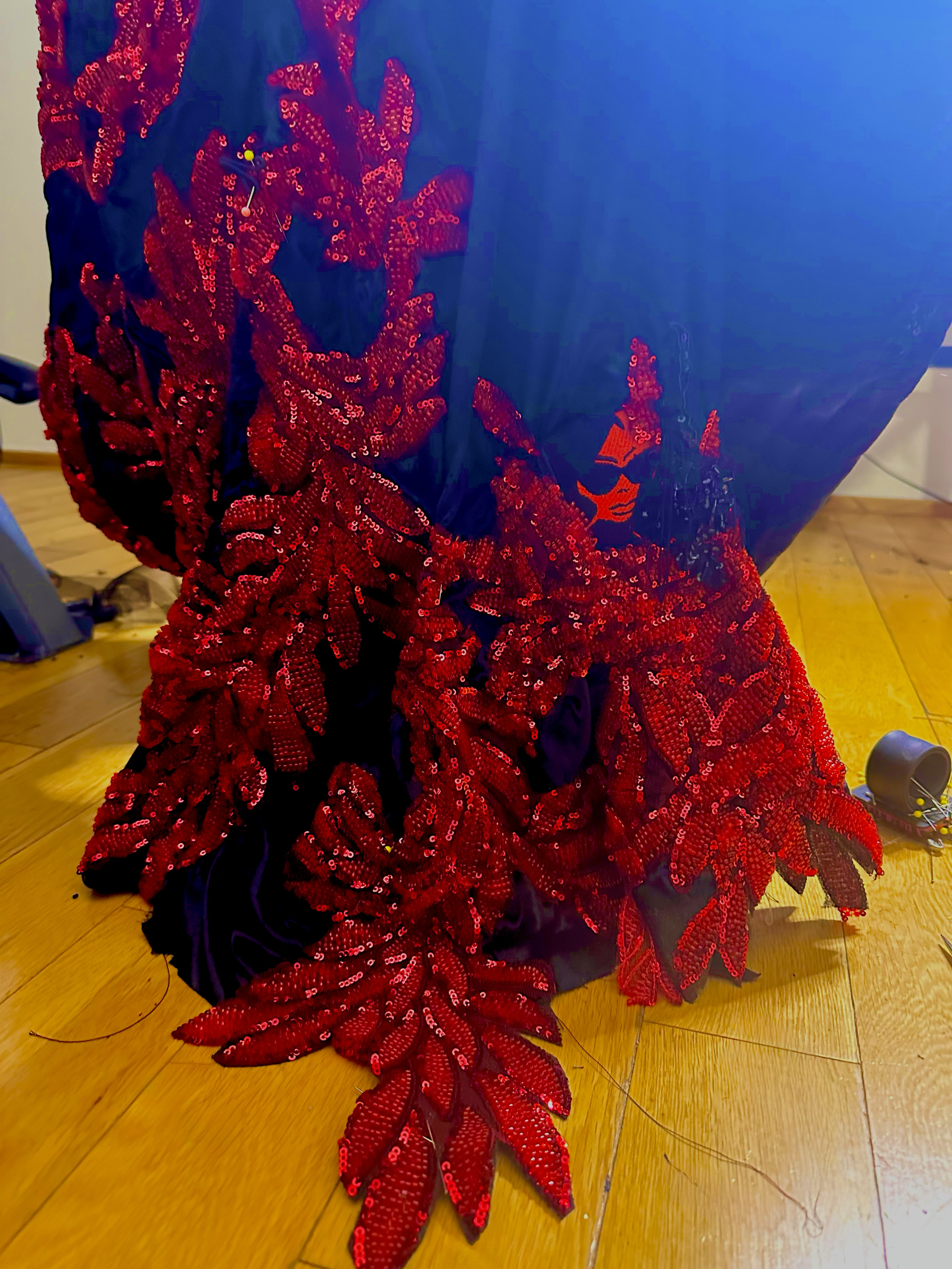 A garment decorated with red sequined leaf patterns on dark fabric, resting on a wooden floor with some toys nearby.