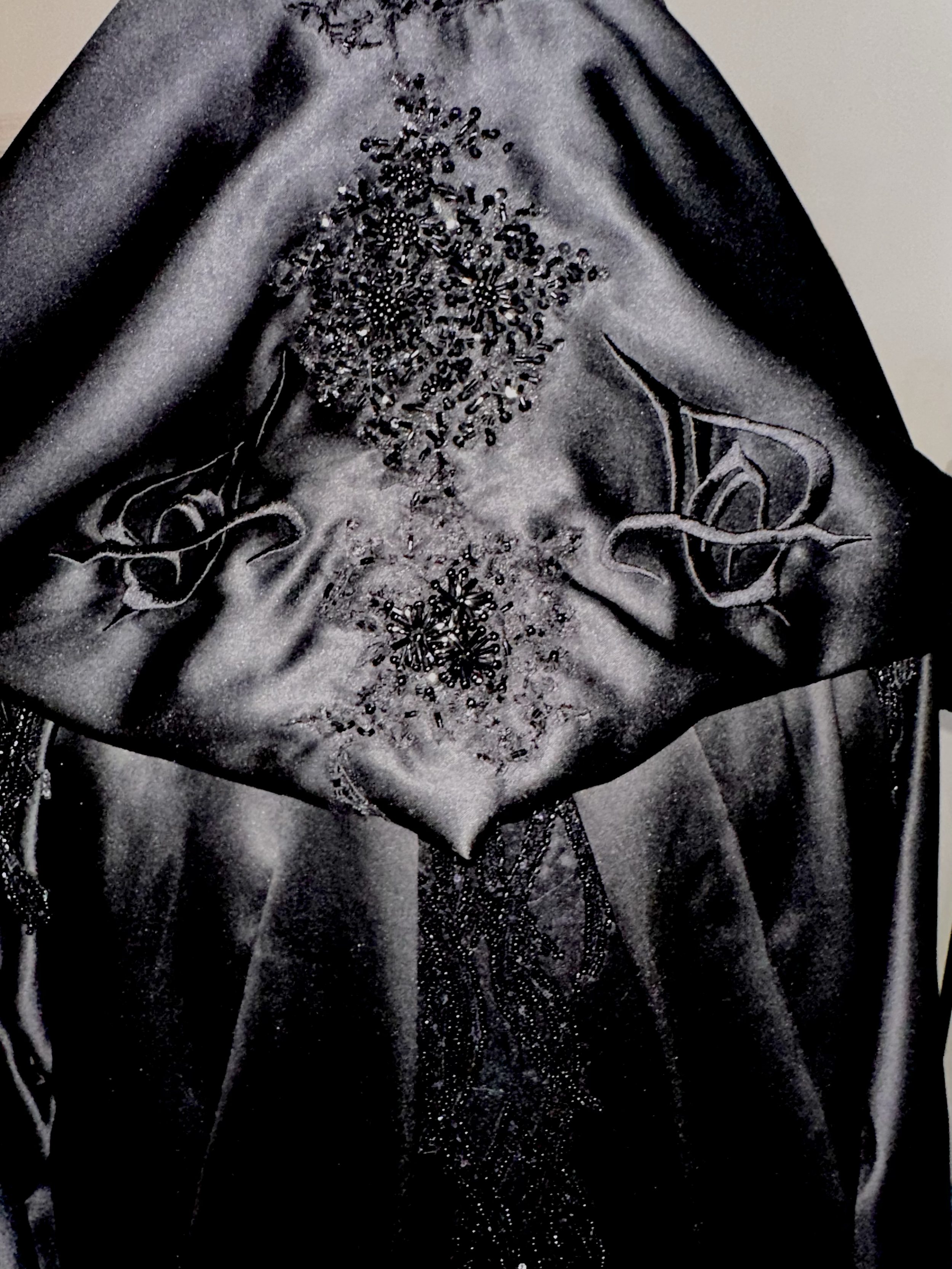 Black satin fabric with intricate bead and embroidery designs, including floral patterns and decorative swirls.