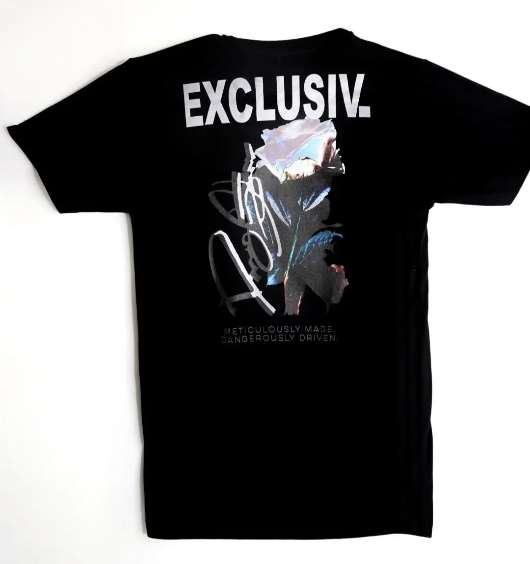Black T-shirt with large white text reading 'EXCLUSIVE' and an artistic graphic of a abstract face with floral and scribble elements, and small text 'Meticulously Made. Dangerously Driven.'