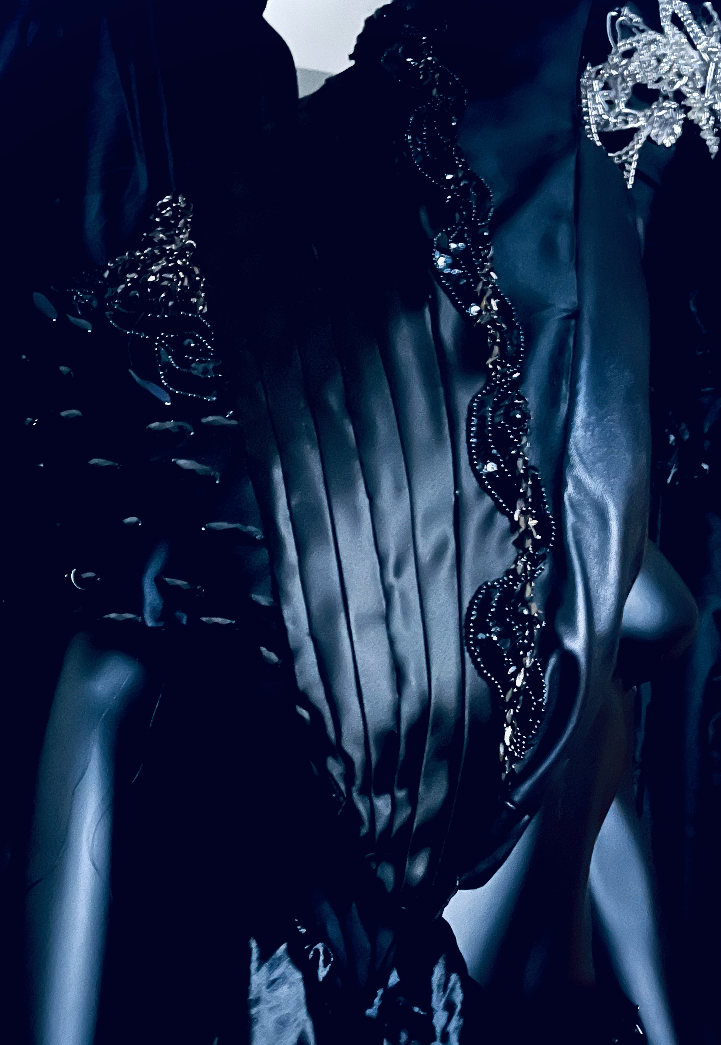 Close-up of a mannequin wearing a black leather jacket with embellished chain detailing and floral embroidery, dark background.