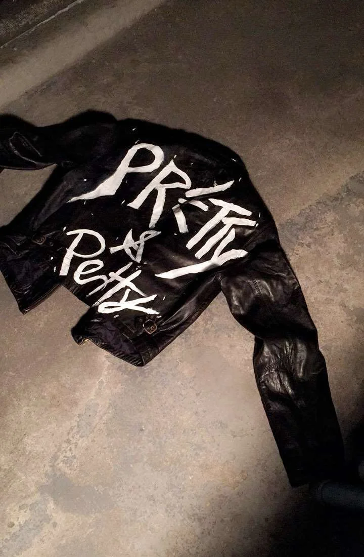 A black jacket with white painted text that reads "PRIVATE & aPex" lying on a concrete ground.