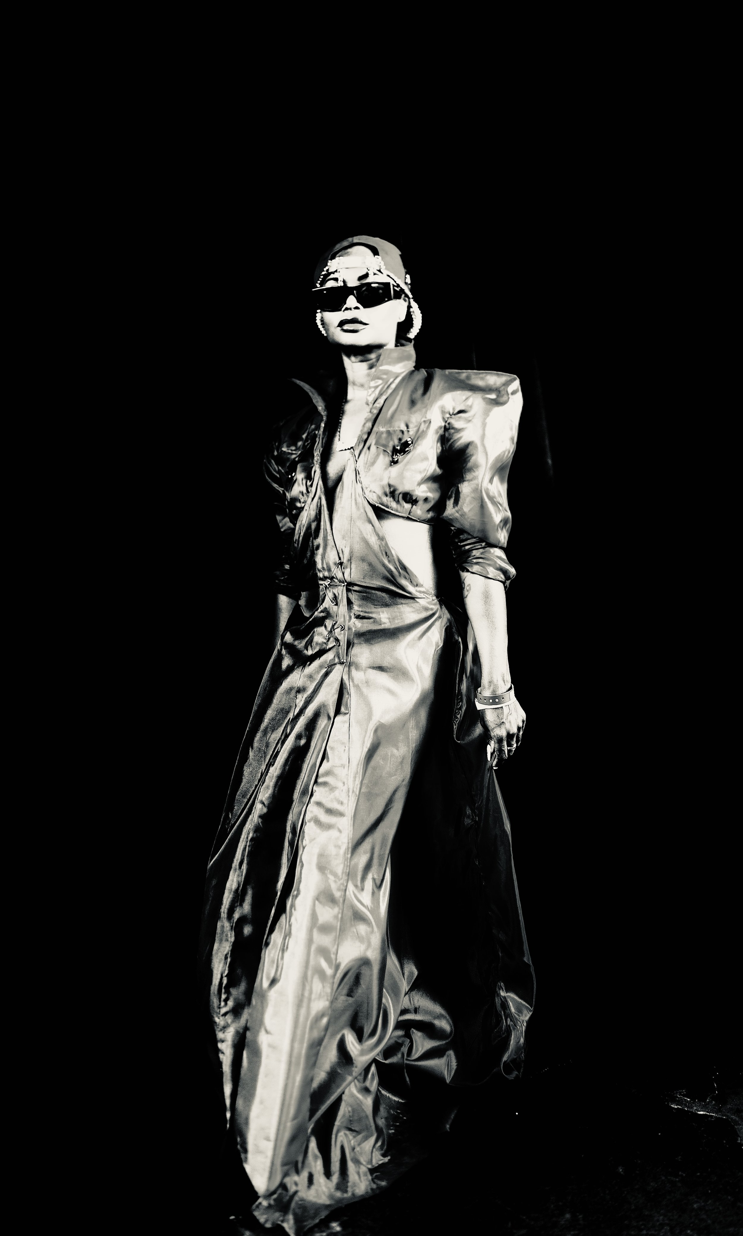 A woman wearing metallic clothing, sunglasses, and a cap, walking against a black background.