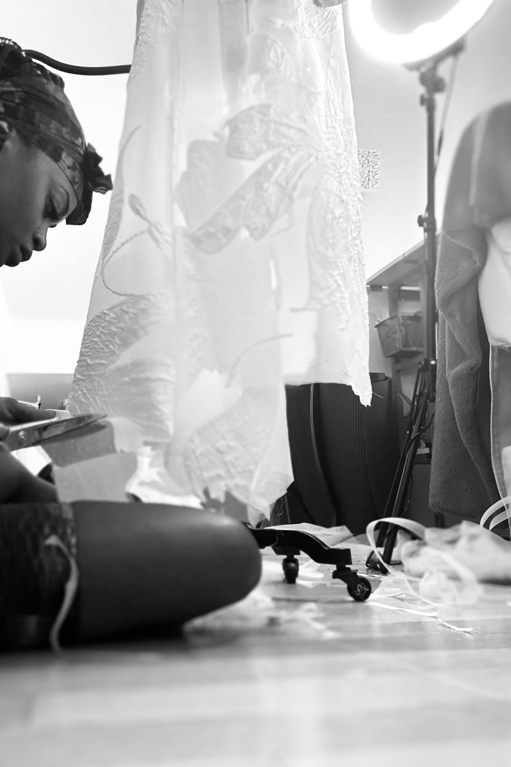 Person with headscarf sitting on the floor, using a smartphone, surrounded by photography equipment and fabric in a studio setting.