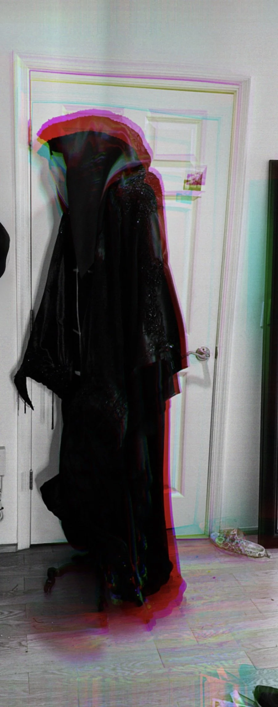 A black coat hanging on a door with a reflection created by digital glitch effects.