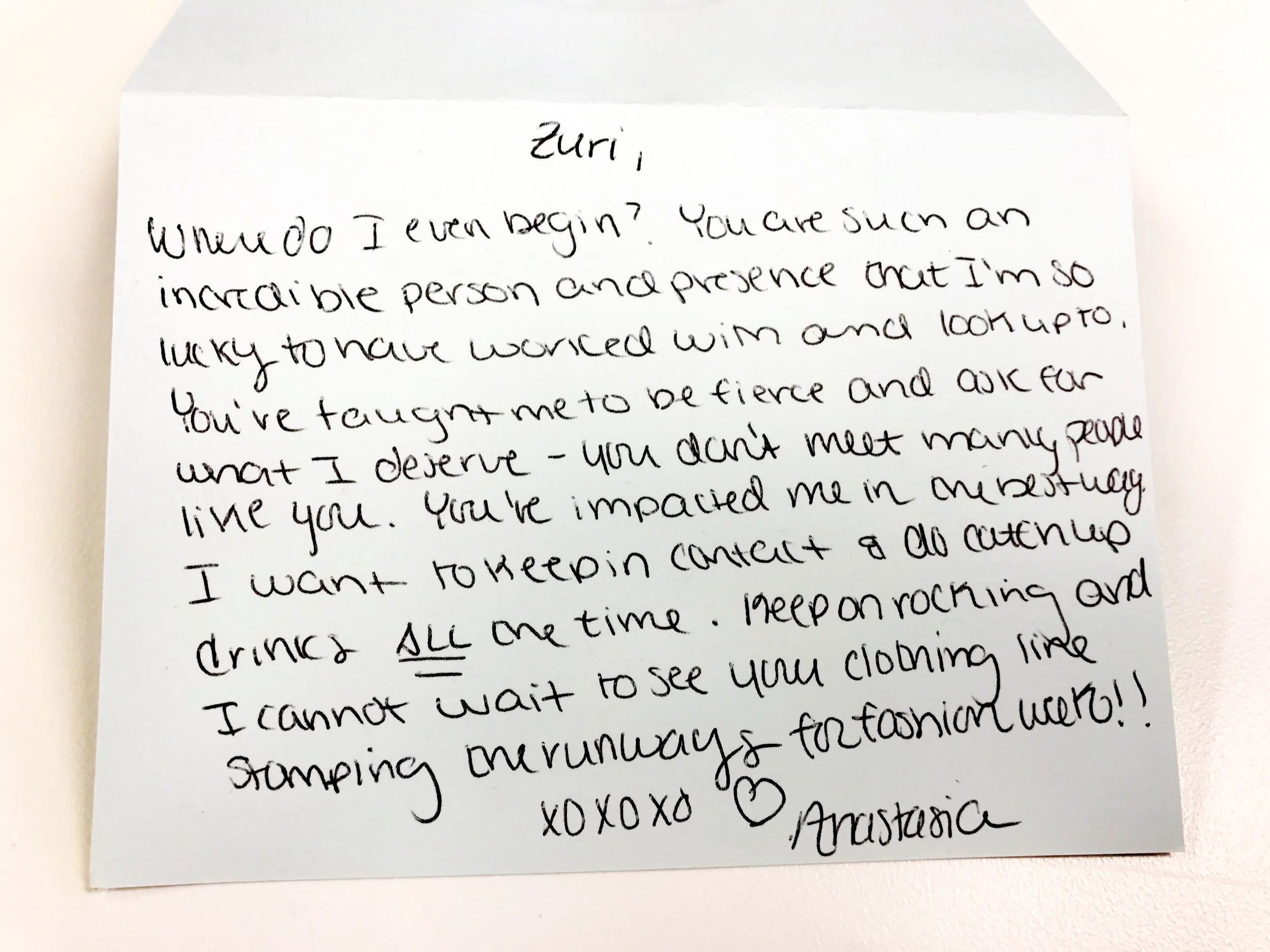 A handwritten note addressed to Zuri on a light-colored paper, expressing admiration and excitement for seeing her clothing and stamping mugshots for a fashion show.