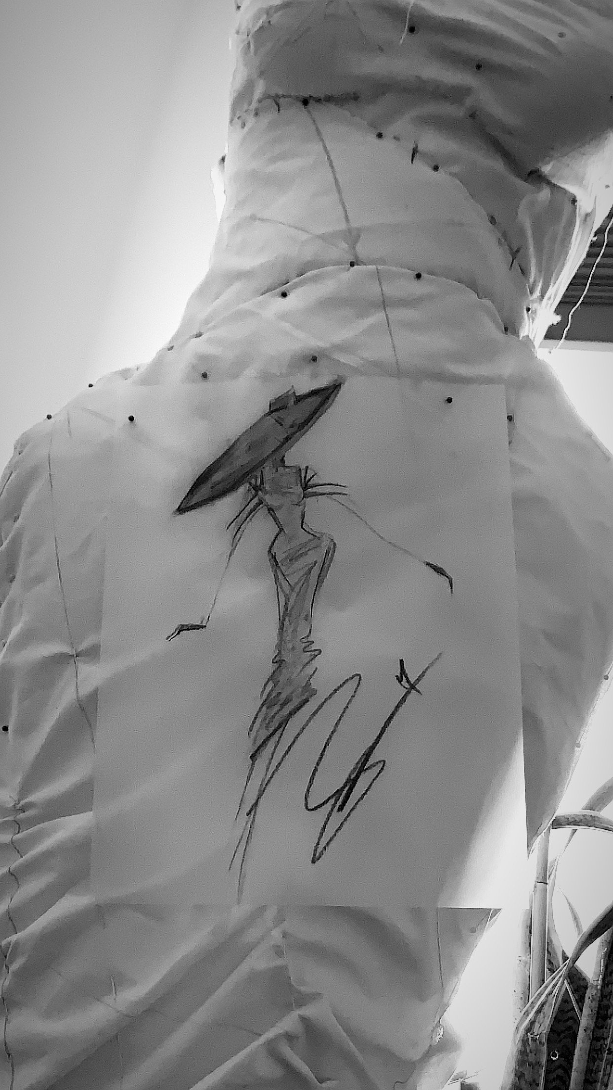 Black and white photo of a person's back with a piece of paper pinned to their clothing. A sketch of a woman with a parasol is drawn on the paper.
