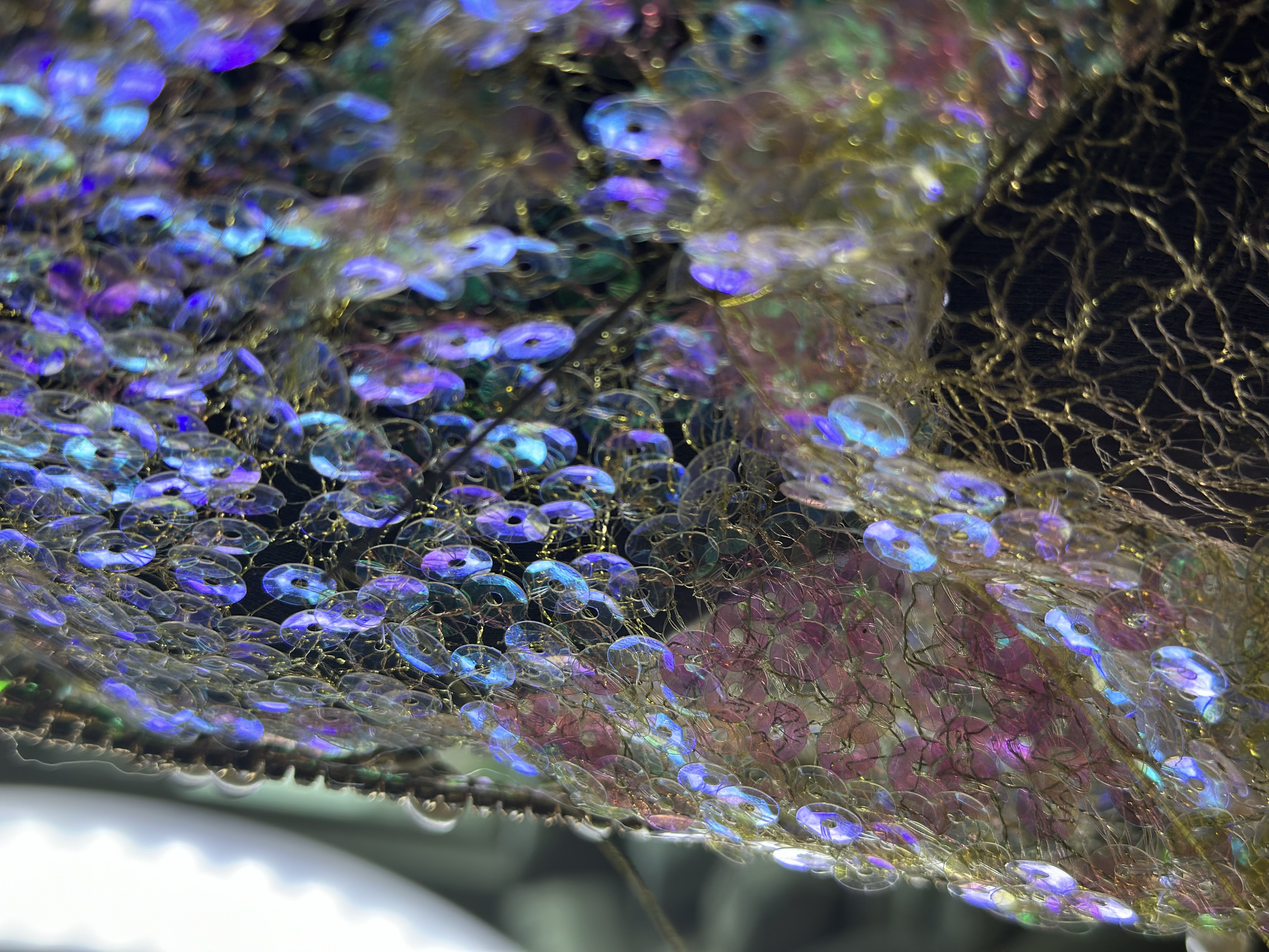 Close-up of iridescent, colorful sequins and mesh fabric creating a shimmering, abstract pattern.