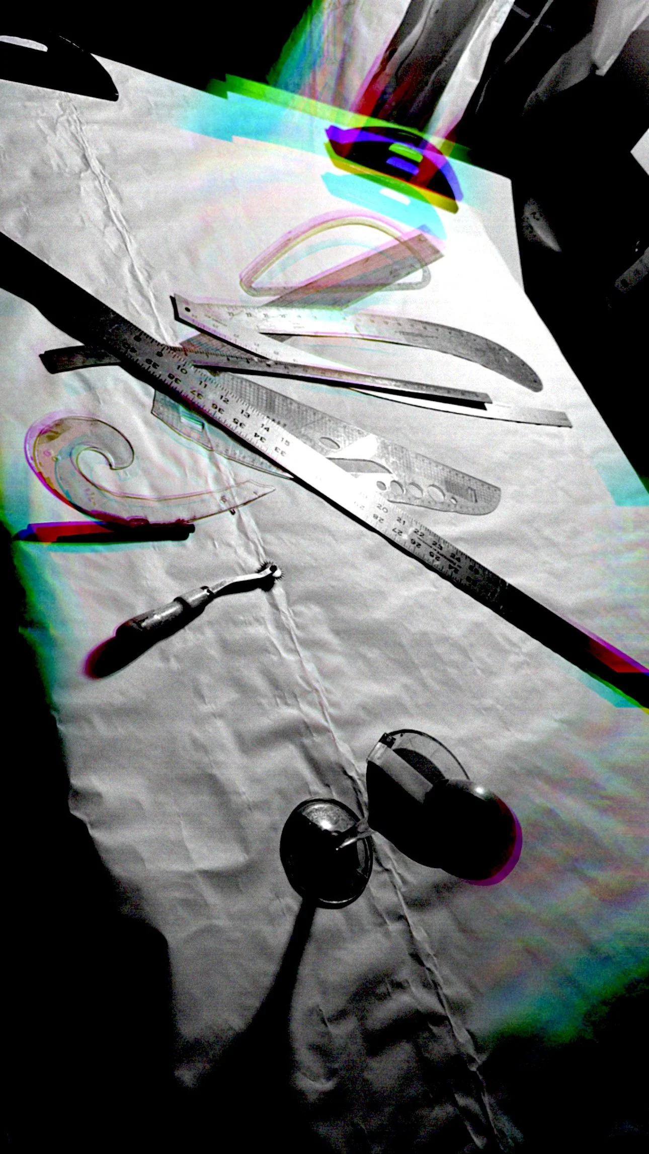 Tools including a ruler, caliper, curved plastic item, and adjustable clamp arranged on a white fabric surface, with some parts distorted and color effects.