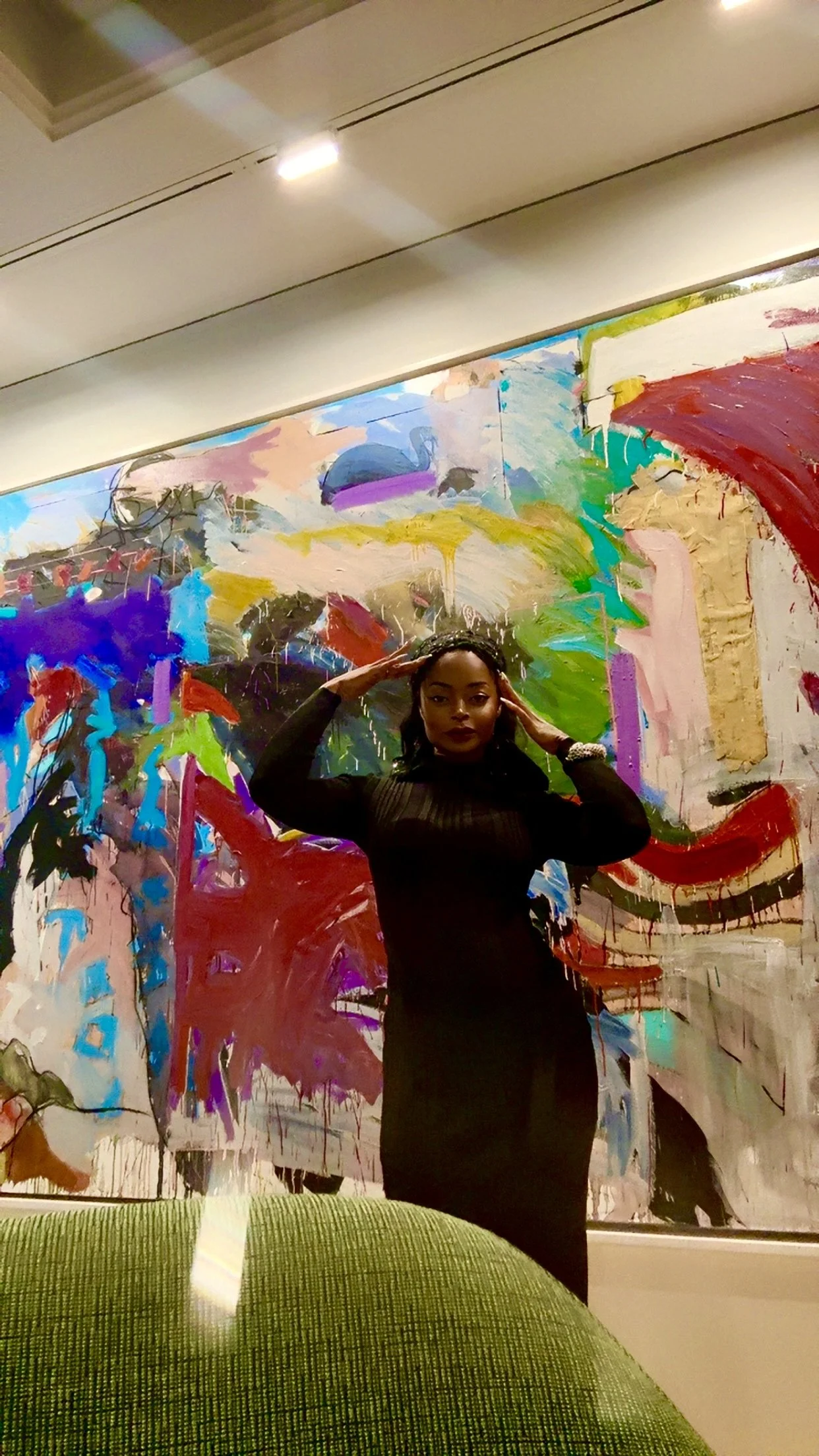 A woman in a black dress posing in front of an abstract colorful painting at an art gallery.
