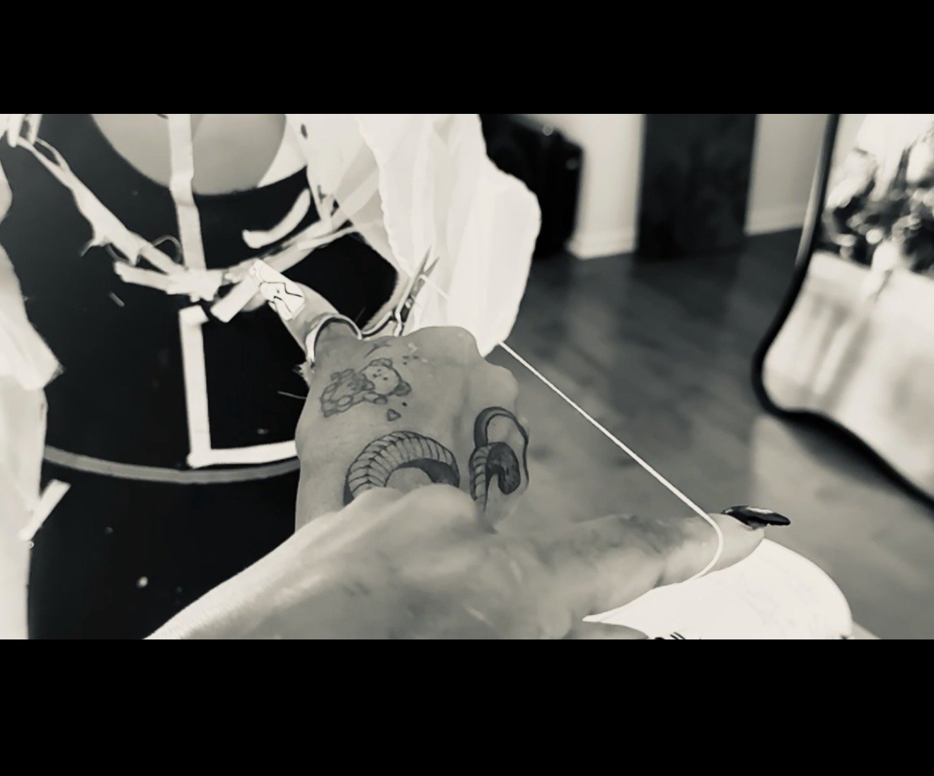 A person with tattoos on their hand and arm holding a needle, preparing to tattoo a design on someone else's skin.