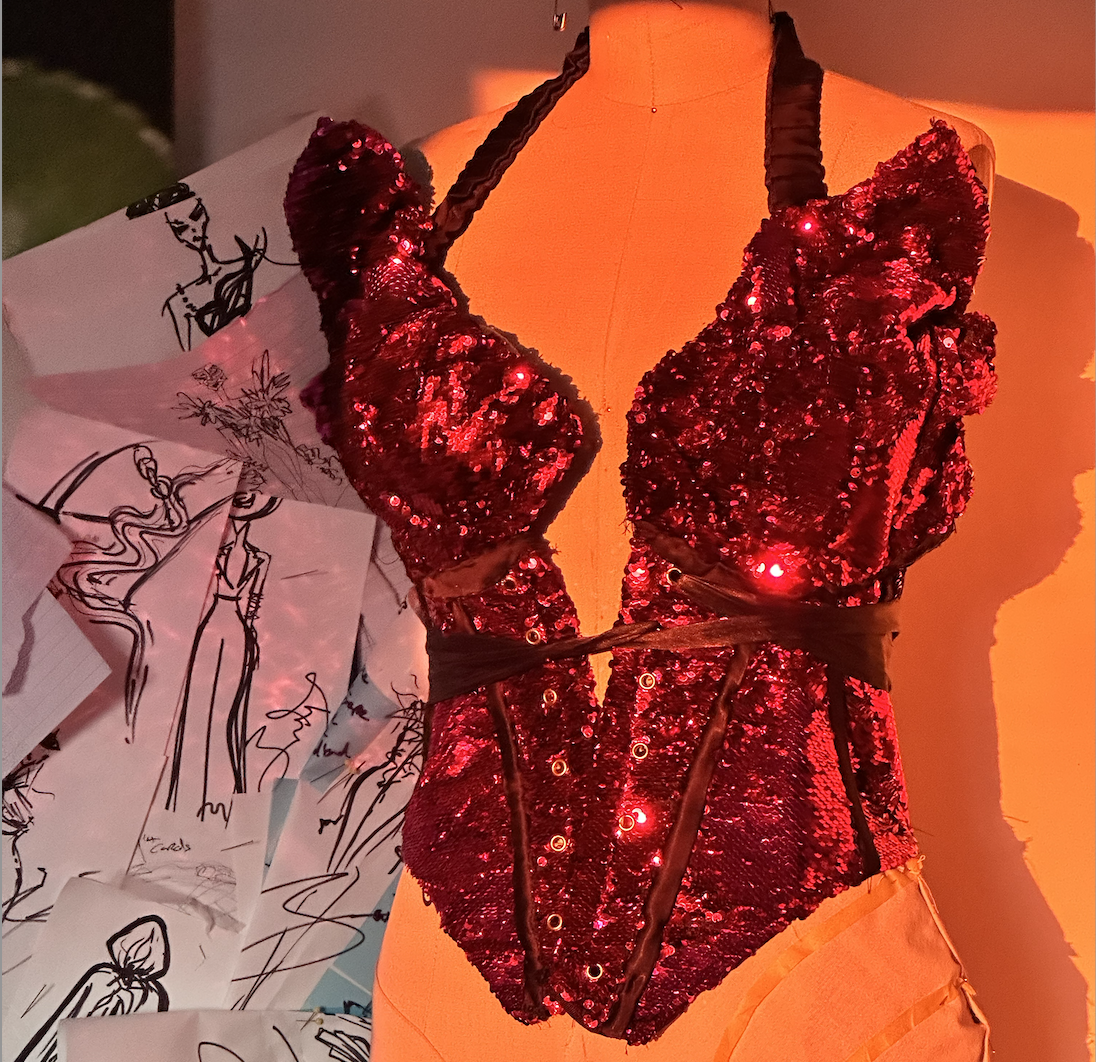 A red sequined dress with black straps displayed on an orange mannequin.