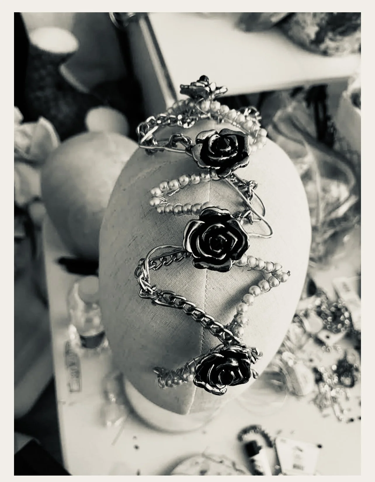 Silver bracelet with black rose designs draped over a mannequin head display, surrounded by various jewelry items in the background.
