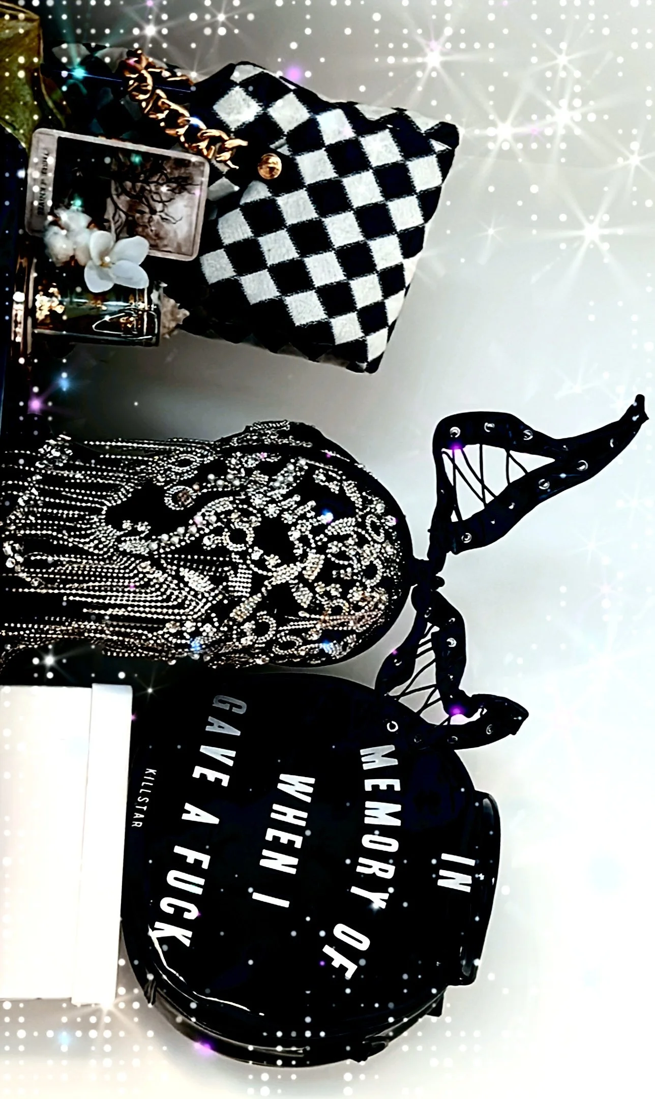 Two large handbags, one with black and white checkerboard pattern and gold chain handle, and the other black with intricate white and pearl embellishments and a bow, placed on a white surface with decorative items and a sign that reads 'IN MEMORI OF'