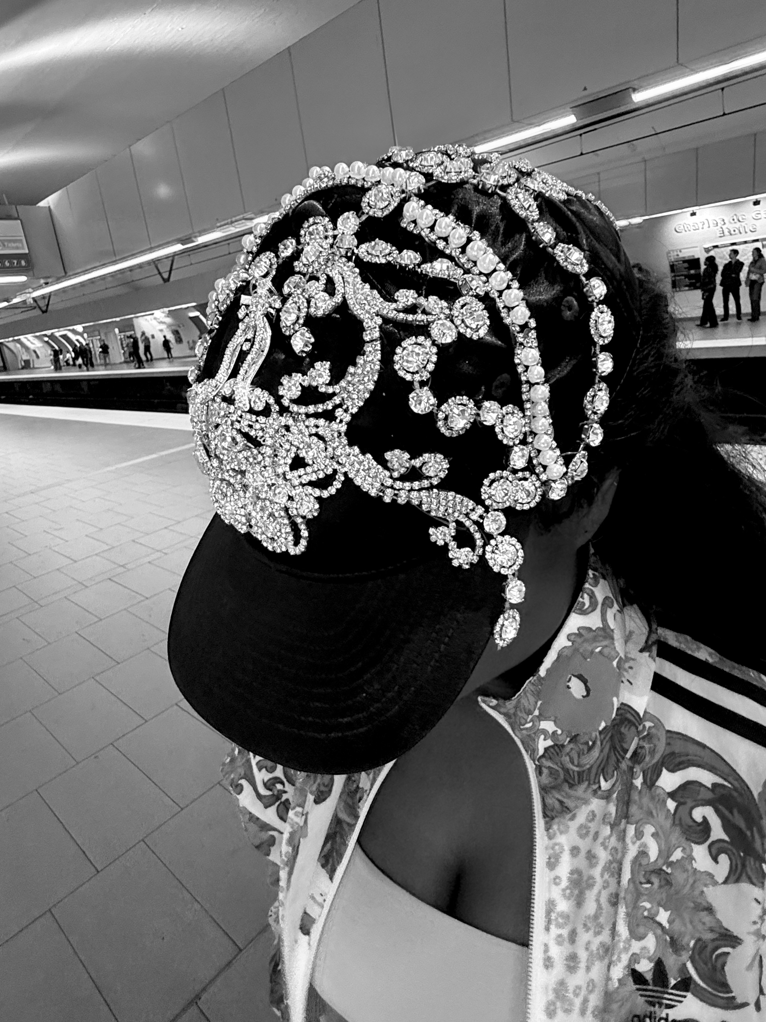Person wearing a black cap decorated with numerous diamonds, standing at a subway station.