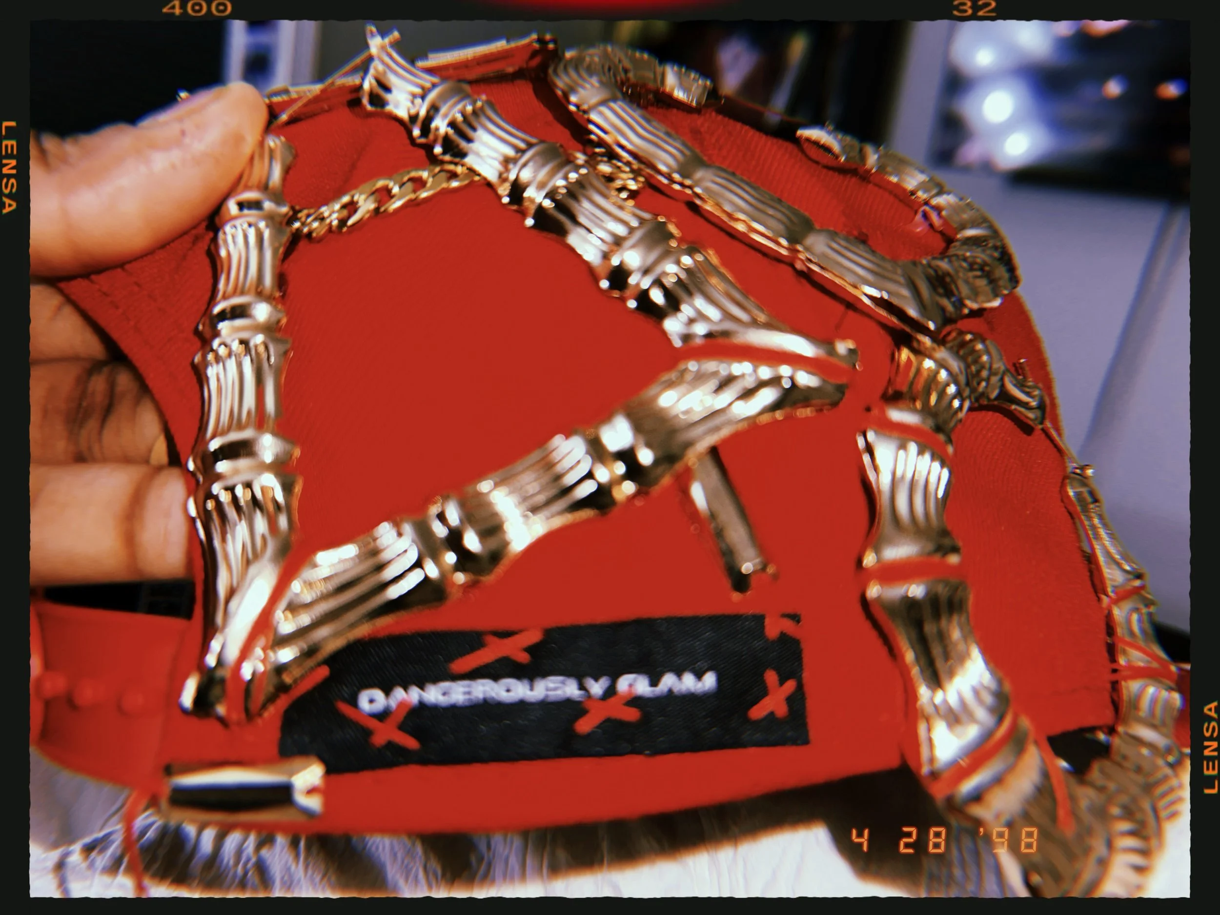 A red jewelry box with a black label that reads 'DANGEROUSLY GLAM' and two gold chains with decorative bars inside.