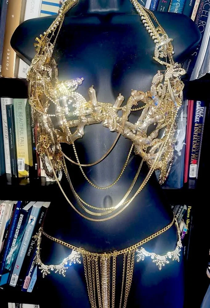 Gold jewelry necklace and body chain displayed on a black mannequin torso, with bookshelves in the background.