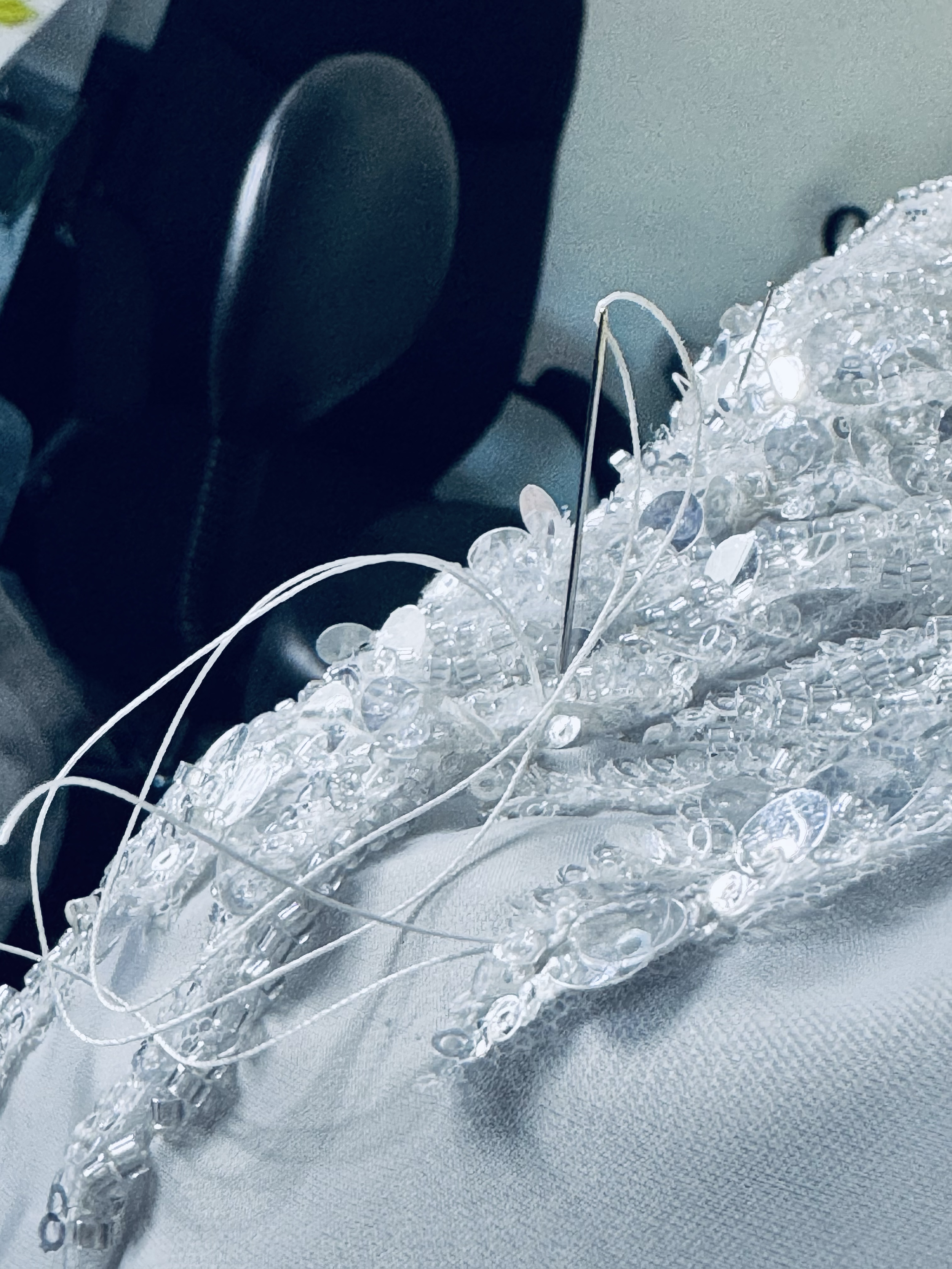 A close-up of a decorative headpiece made of clear beads, pearls, and silver wires resting on a light-colored fabric surface inside a vehicle.