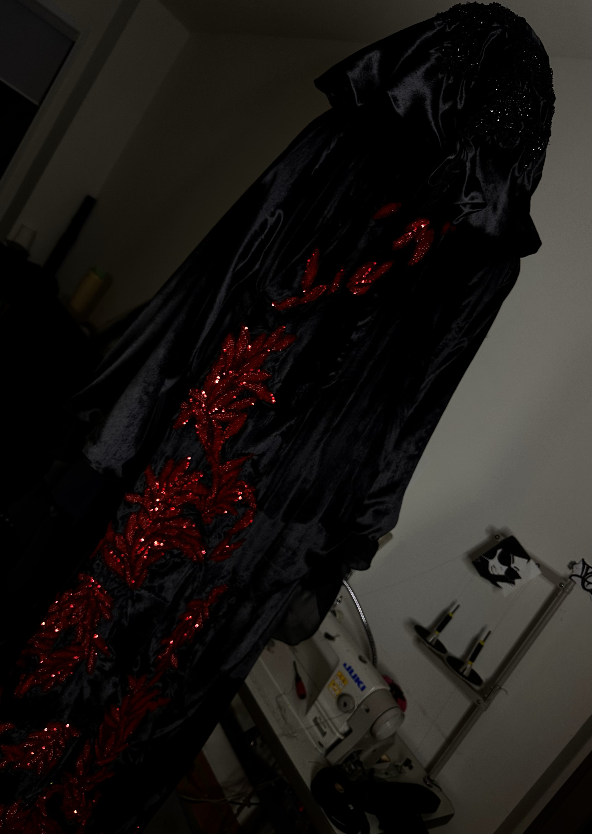 A black velvet garment with red sequined floral embroidery, displayed on a mannequin in a craft room.