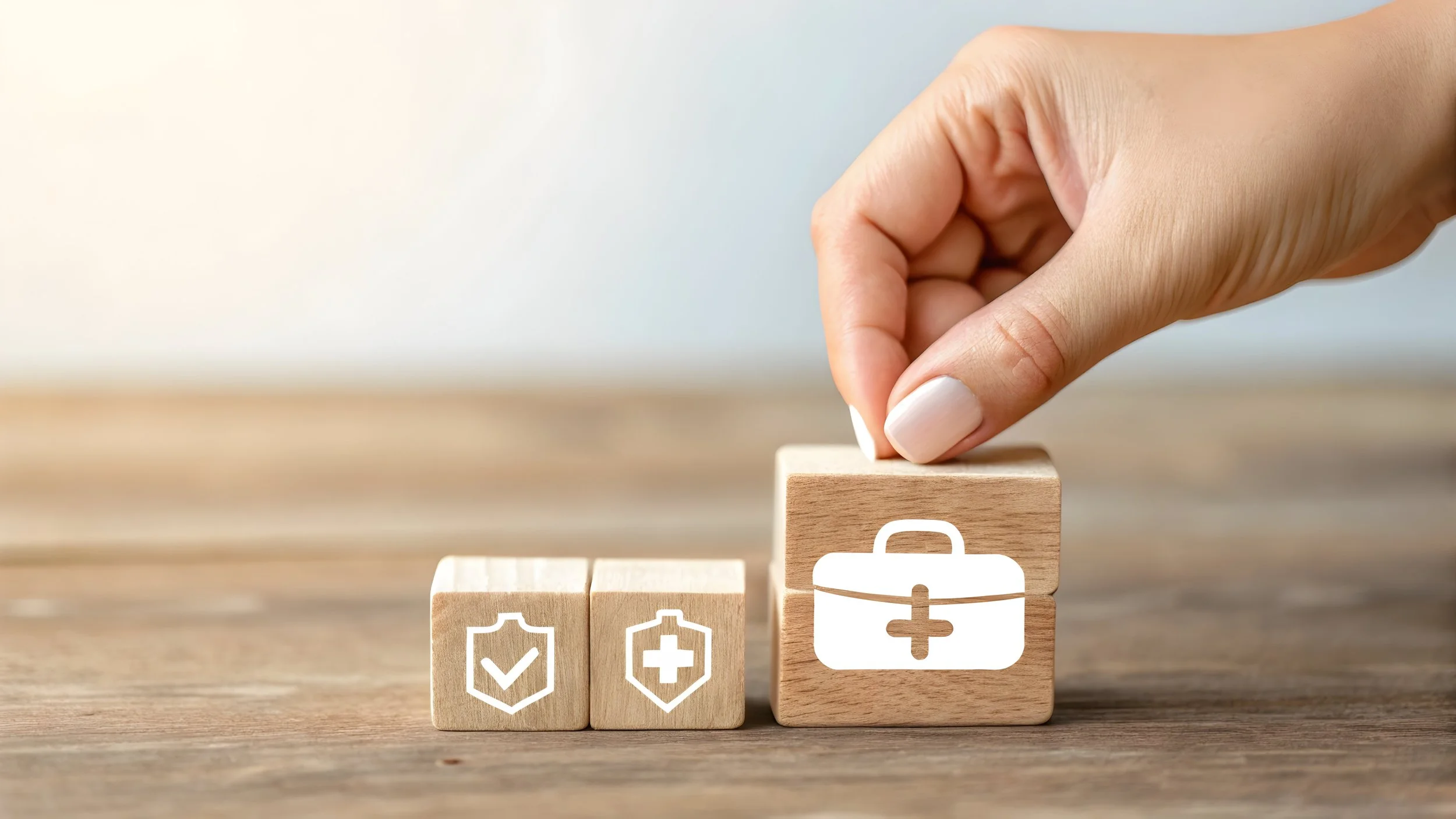A hand is placing a wooden block with a medical kit icon on top of a wooden surface, with two smaller blocks with health icons in front.