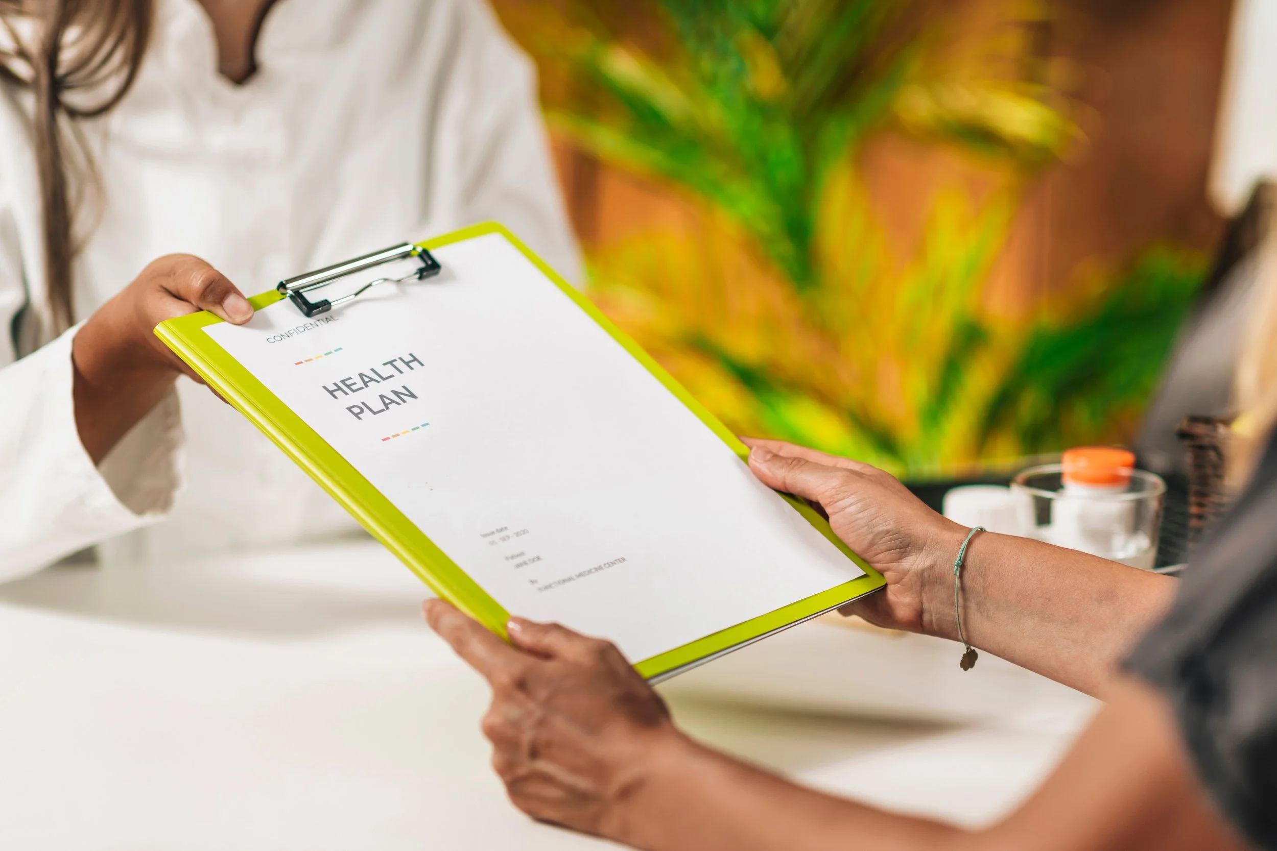 Person handing a health plan clipboard to another person in an office setting with eagerness in the air.