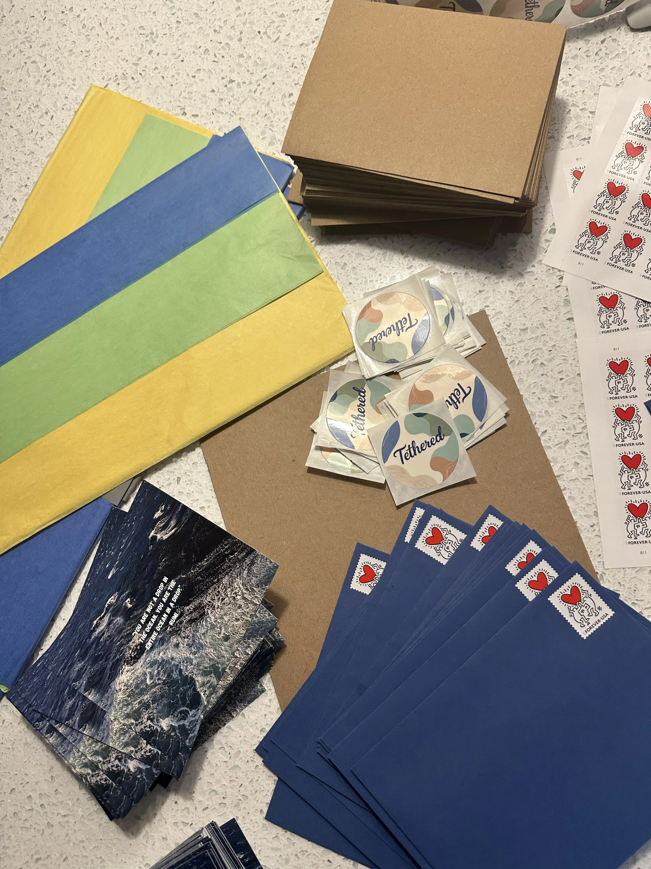 Assorted colorful envelopes and stamps are arranged on a table. Circular Tethered stickers and heart-themed stamps.