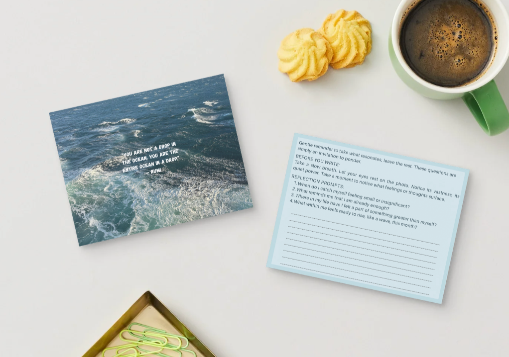 A cup of black coffee sits beside two yellow pastries on a white surface. Nearby, cards display ocean imagery and text.