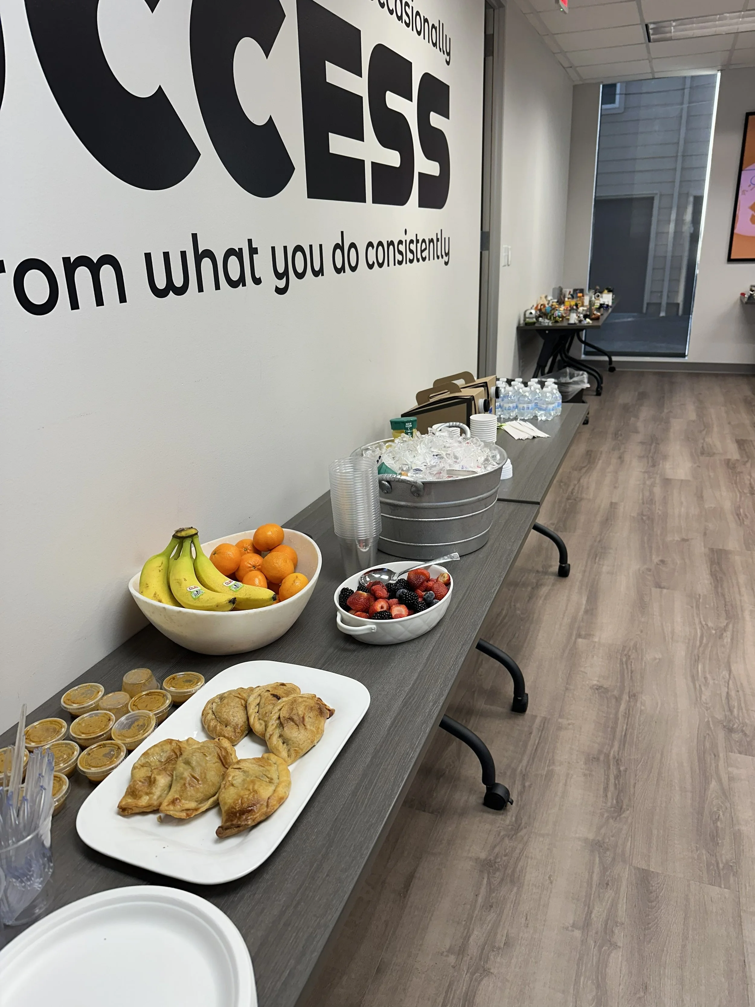 Room with a table of refreshments including fruit, cookies, and drinks; motivational quotes partially visible on the wall.