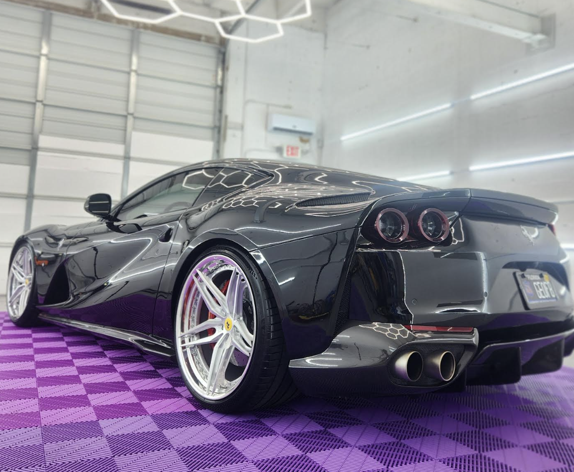 A black Ferrari sports car with purple accents on a purple checkered floor inside a garage or showroom.