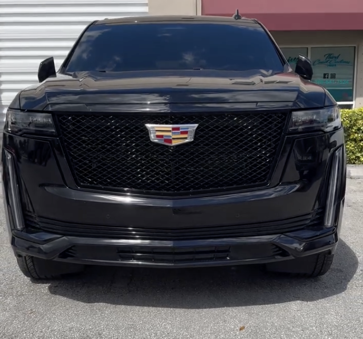 Front view of a black Cadillac SUV with a glossy finish, showing the Cadillac emblem on the grille, parked in front of a building.