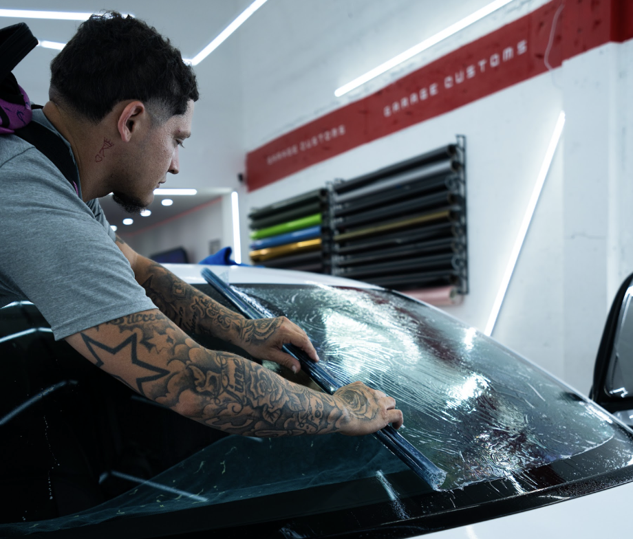 A person with tattoos is installing or replacing a windshield on a car in an auto shop.