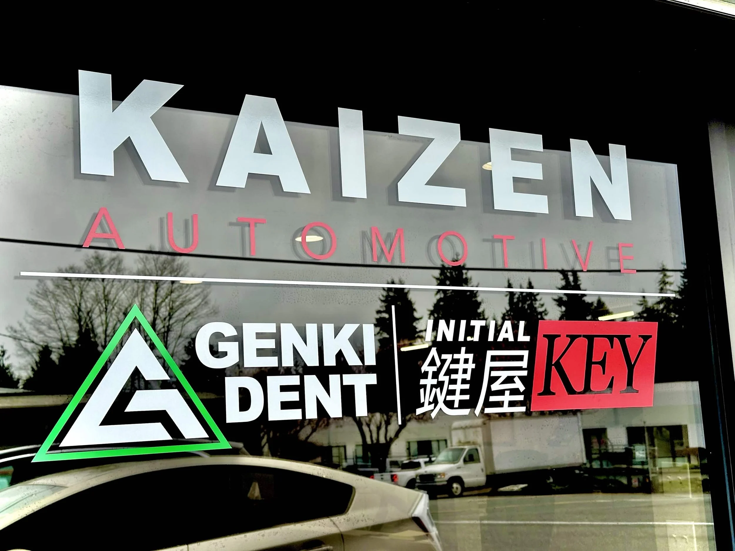 Store window sign for a businesses named 'Genki Dent' with additional signs for 'Kaizen Automotive', and 'Initial Key'.