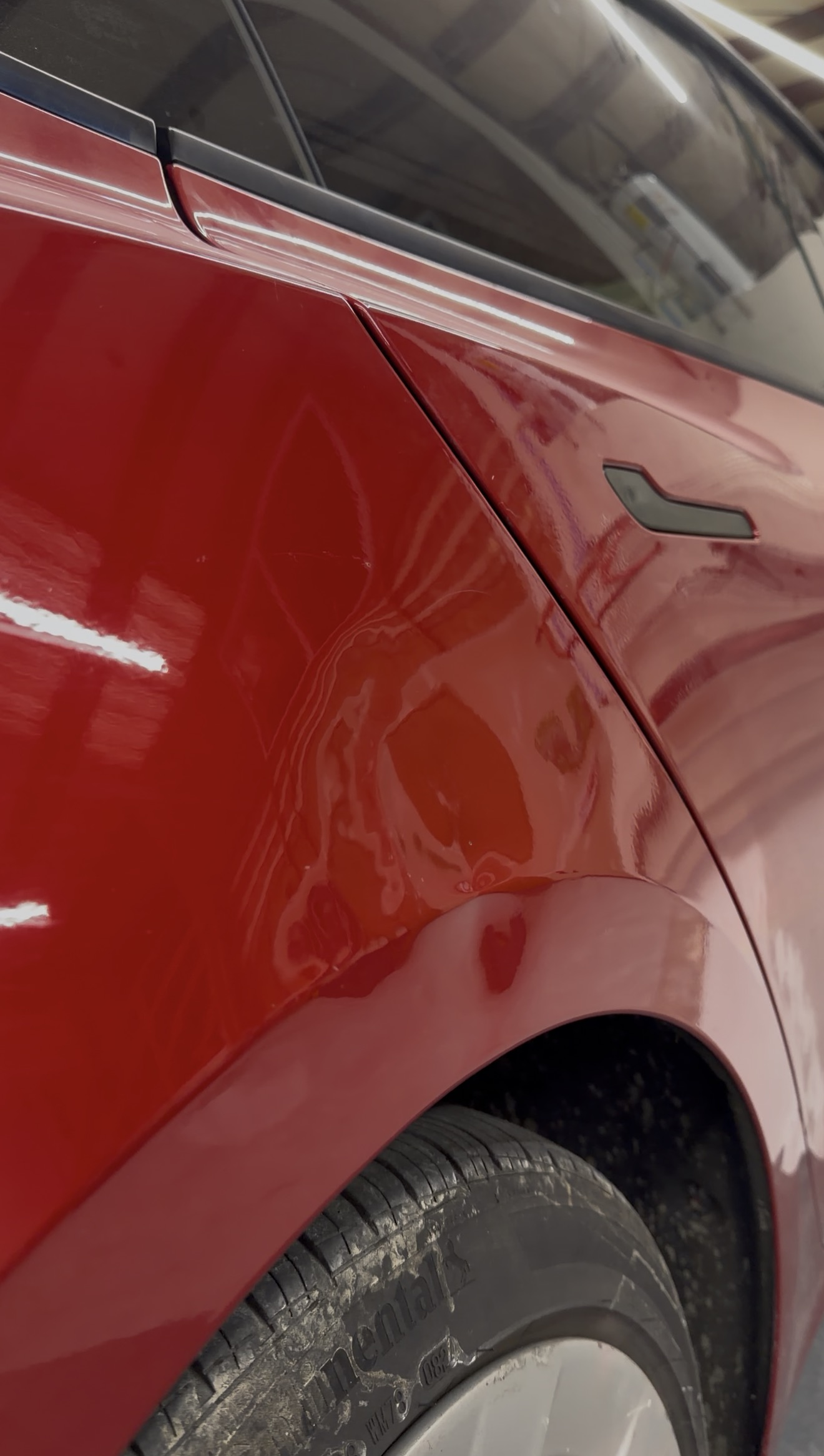 Close-up of a Tesla's rear quarter panel and wheel, with noticeable scratches and dents on the painted surface.