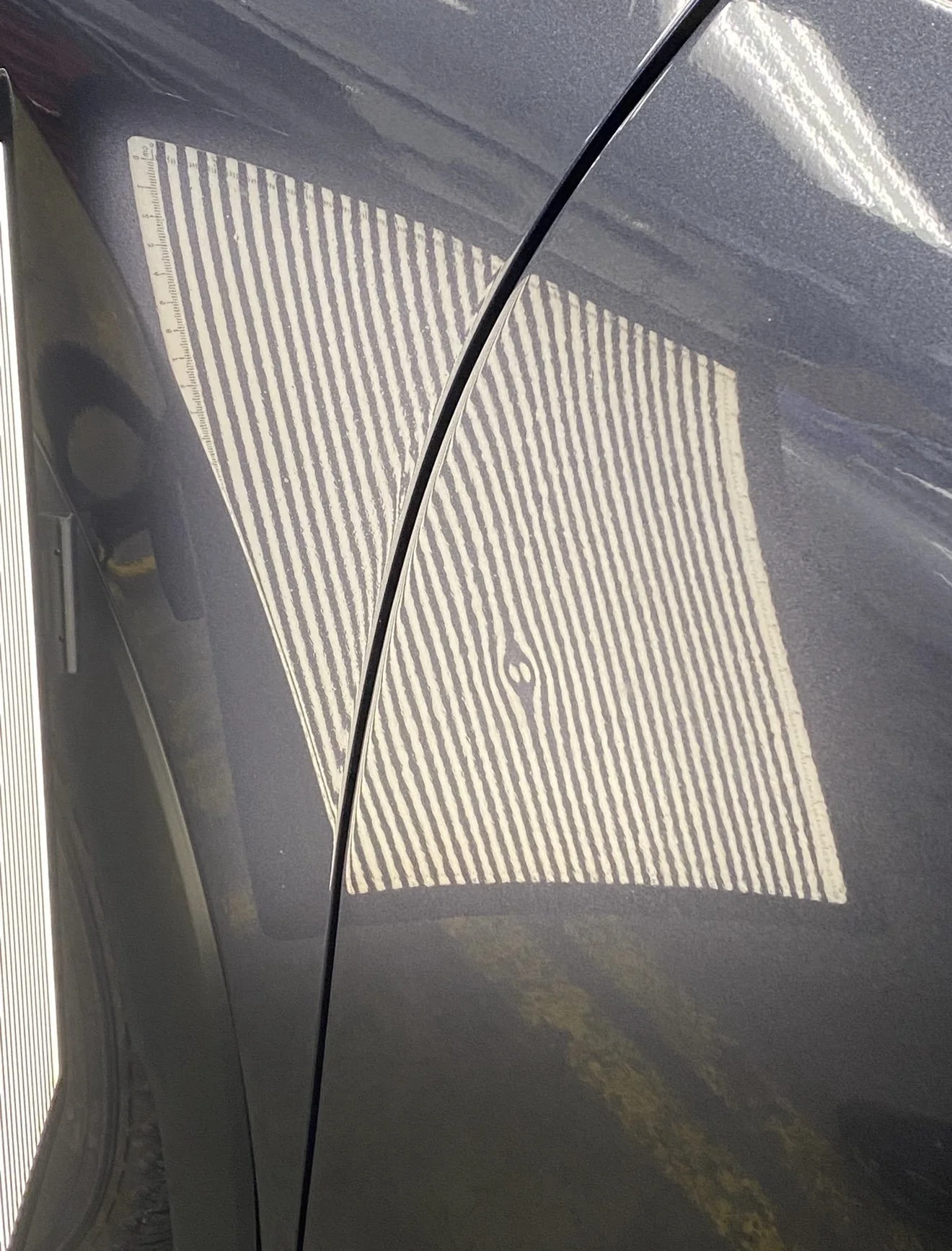 Close-up of the side of a black car with a door ding, line board showing the low-spot on the door.