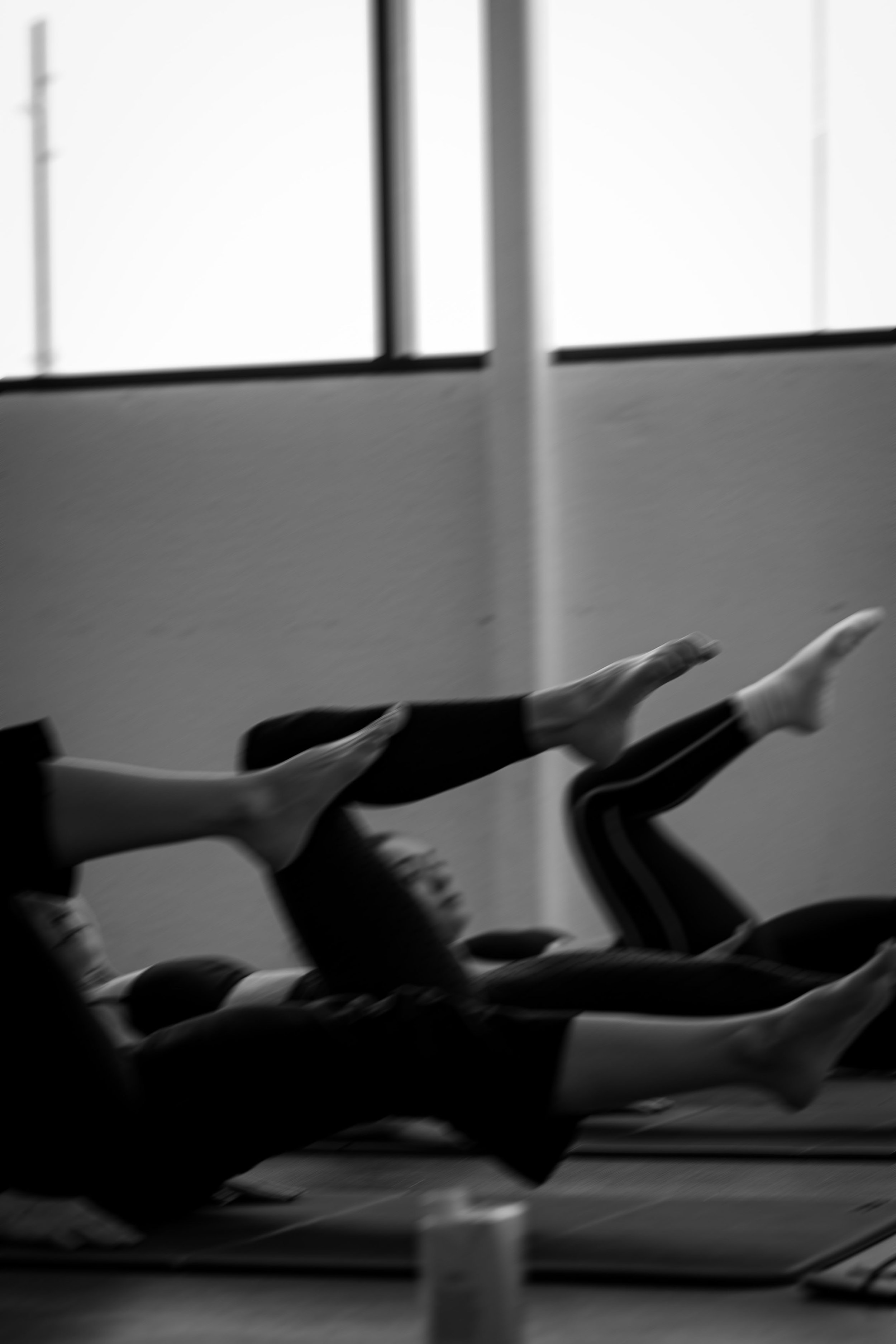 Multiple rowers in a boat practicing rowing indoors, visible through large windows.