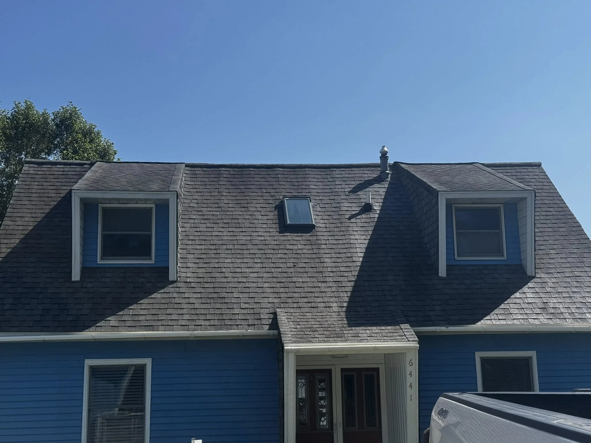 Blue house with two dormer windows on the roof, and a skylight window, under clear blue sky.