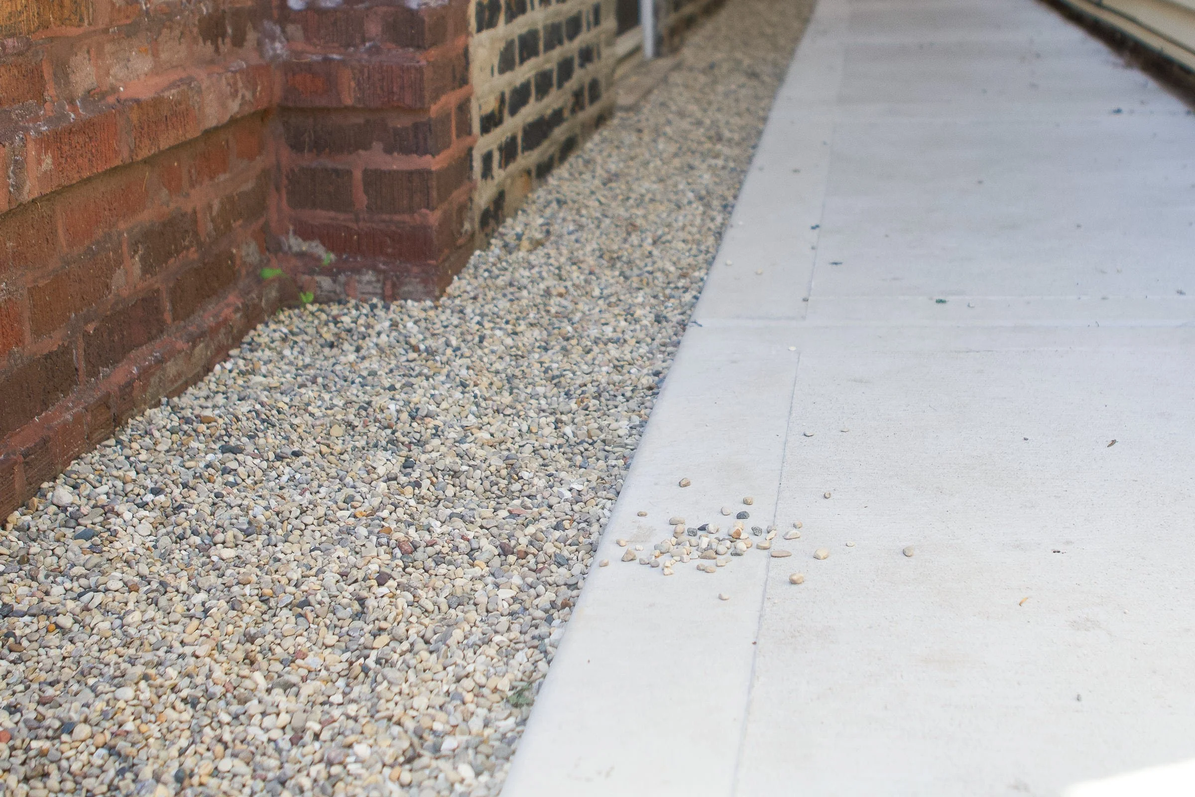 Close-up of a sidewalk and gravel border next to a brick wall.