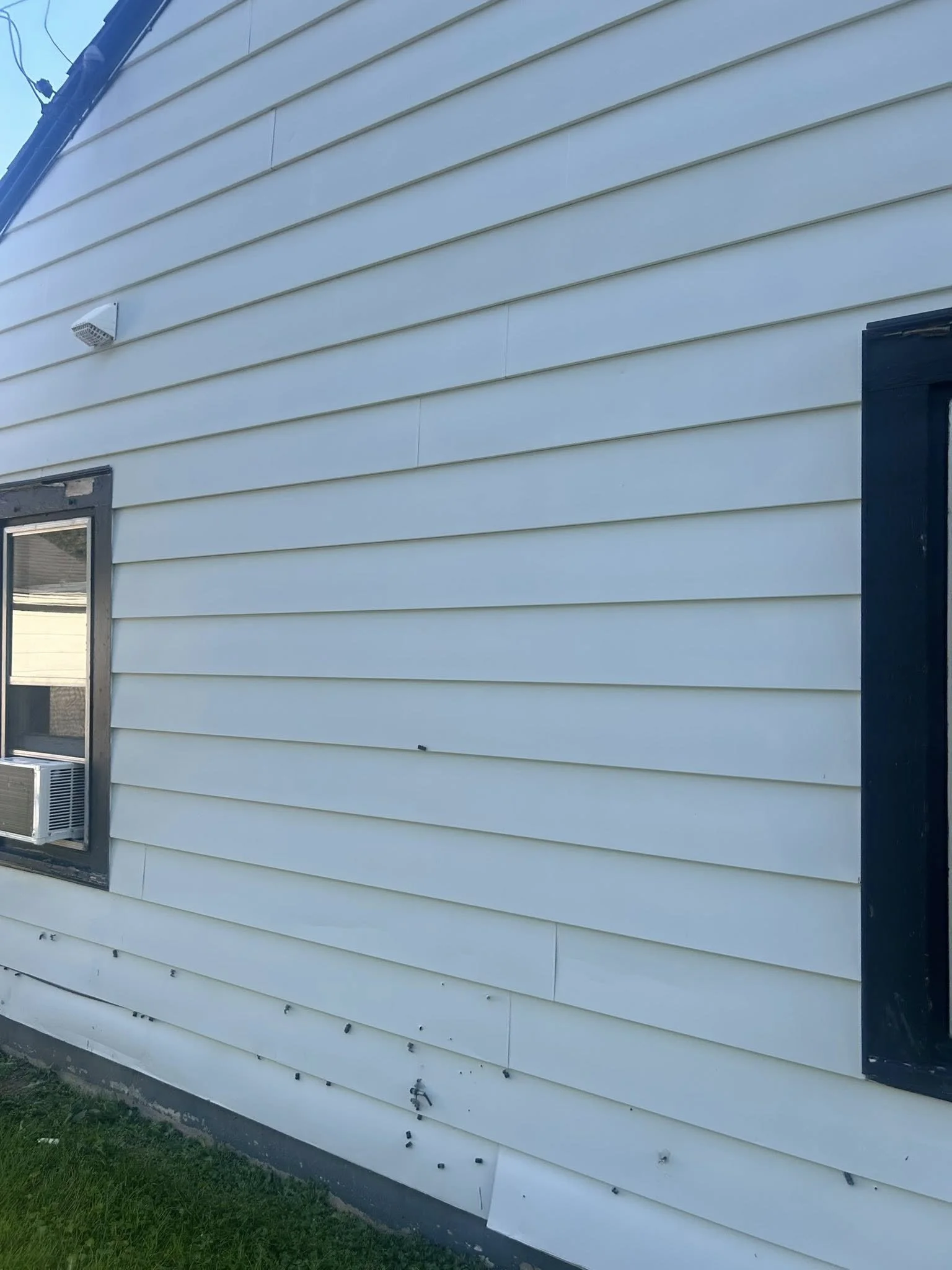 Side of a house with white horizontal siding, a black window frame, and an air conditioning unit in the window.