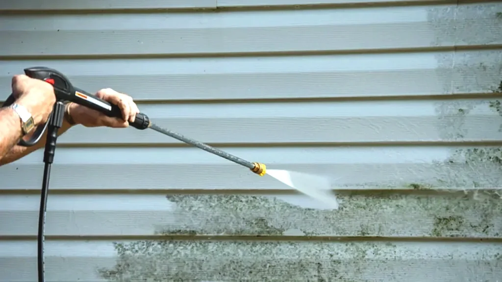 A person using a pressure washer to clean a house's horizontal vinyl siding.